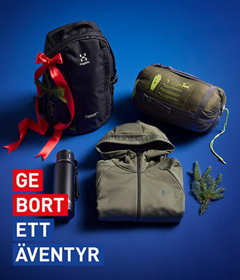 Outdoor gear gift set including a black backpack with a red bow, a green sleeping bag, a hooded jacket, and a thermos, on a blue background with the text "GE BORT ETT ÄVENTYR".