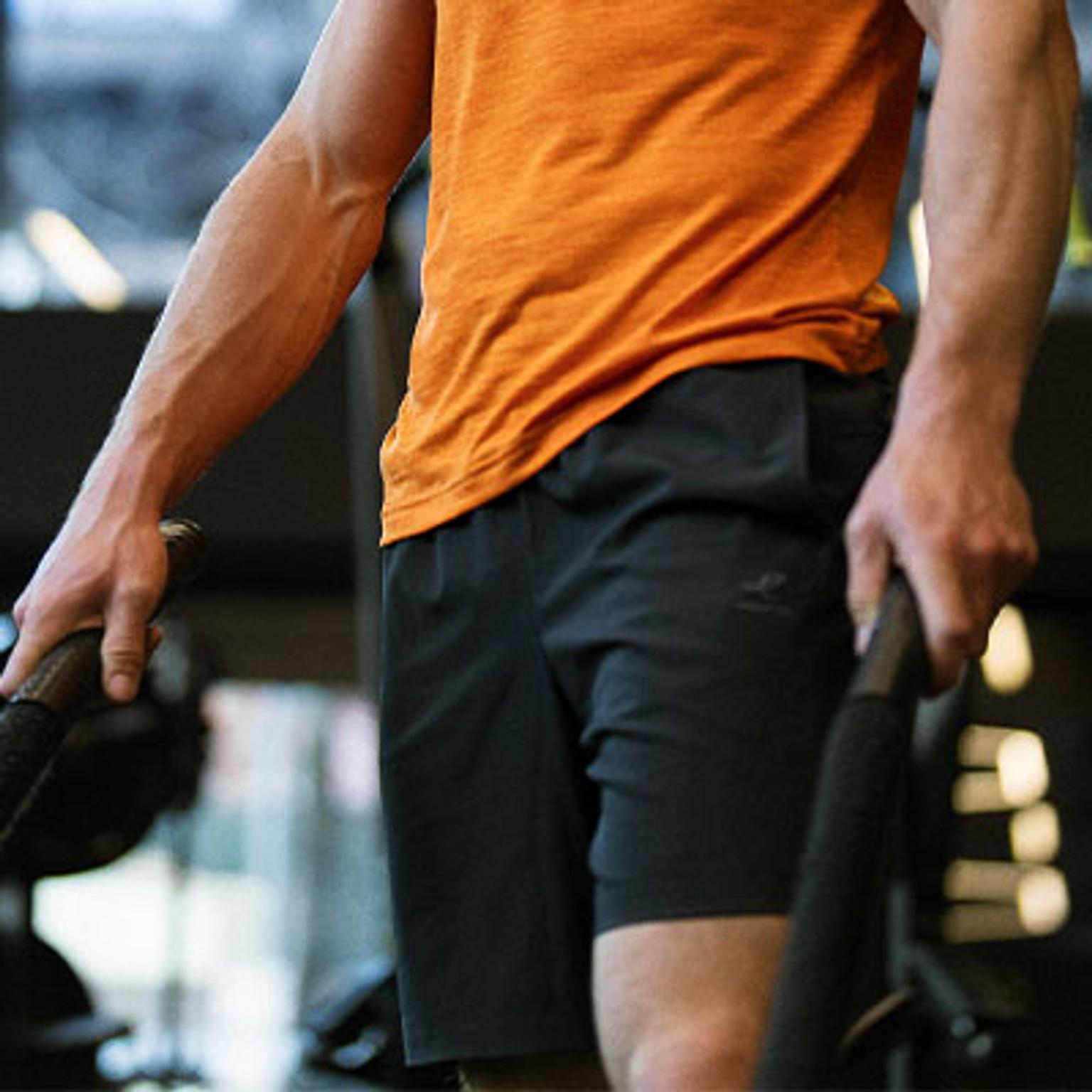 a man in an orange shirt and black shorts is holding a barbell in a gym .
