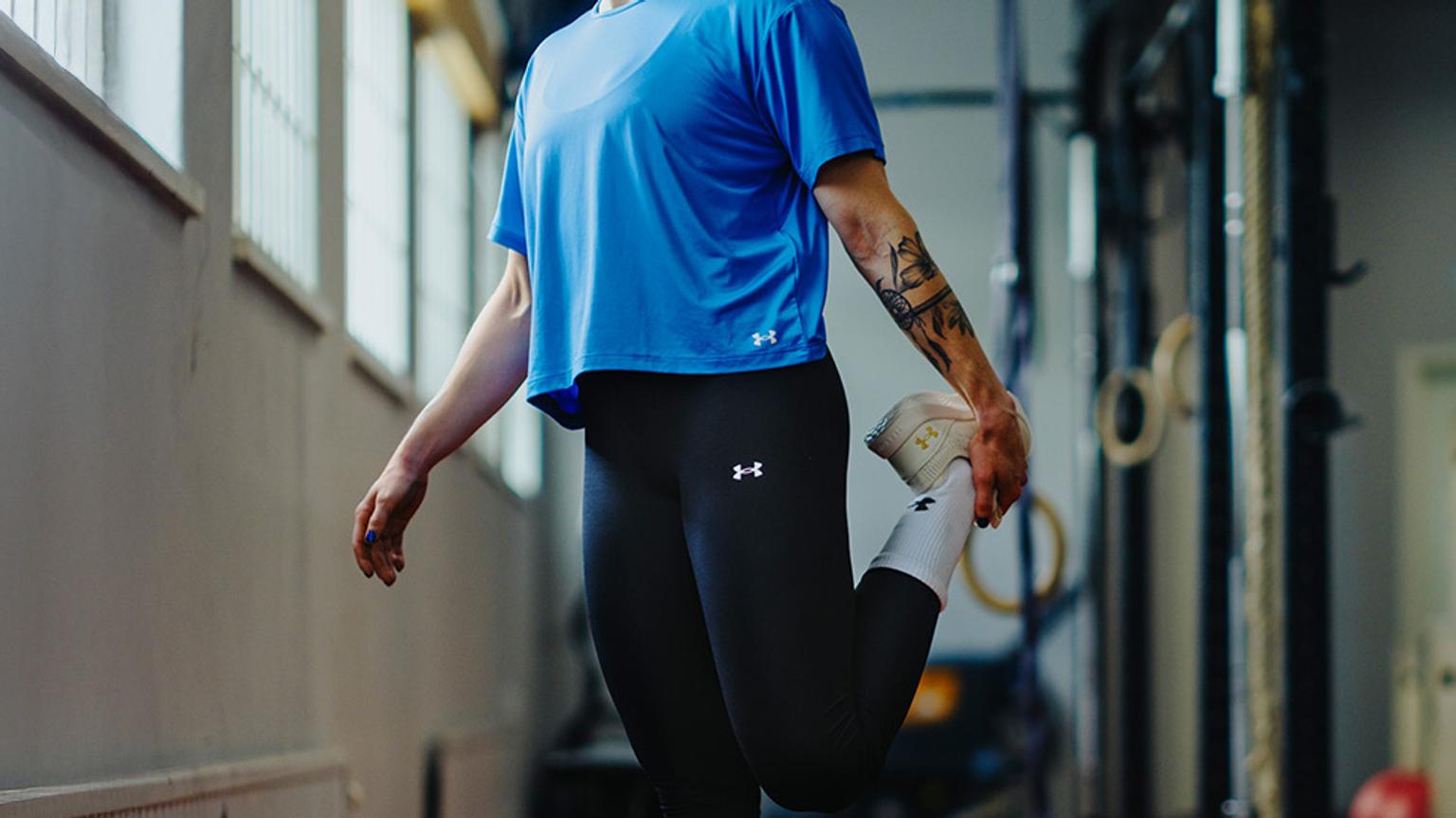 a woman in a blue shirt and black leggings is stretching her leg in a gym .