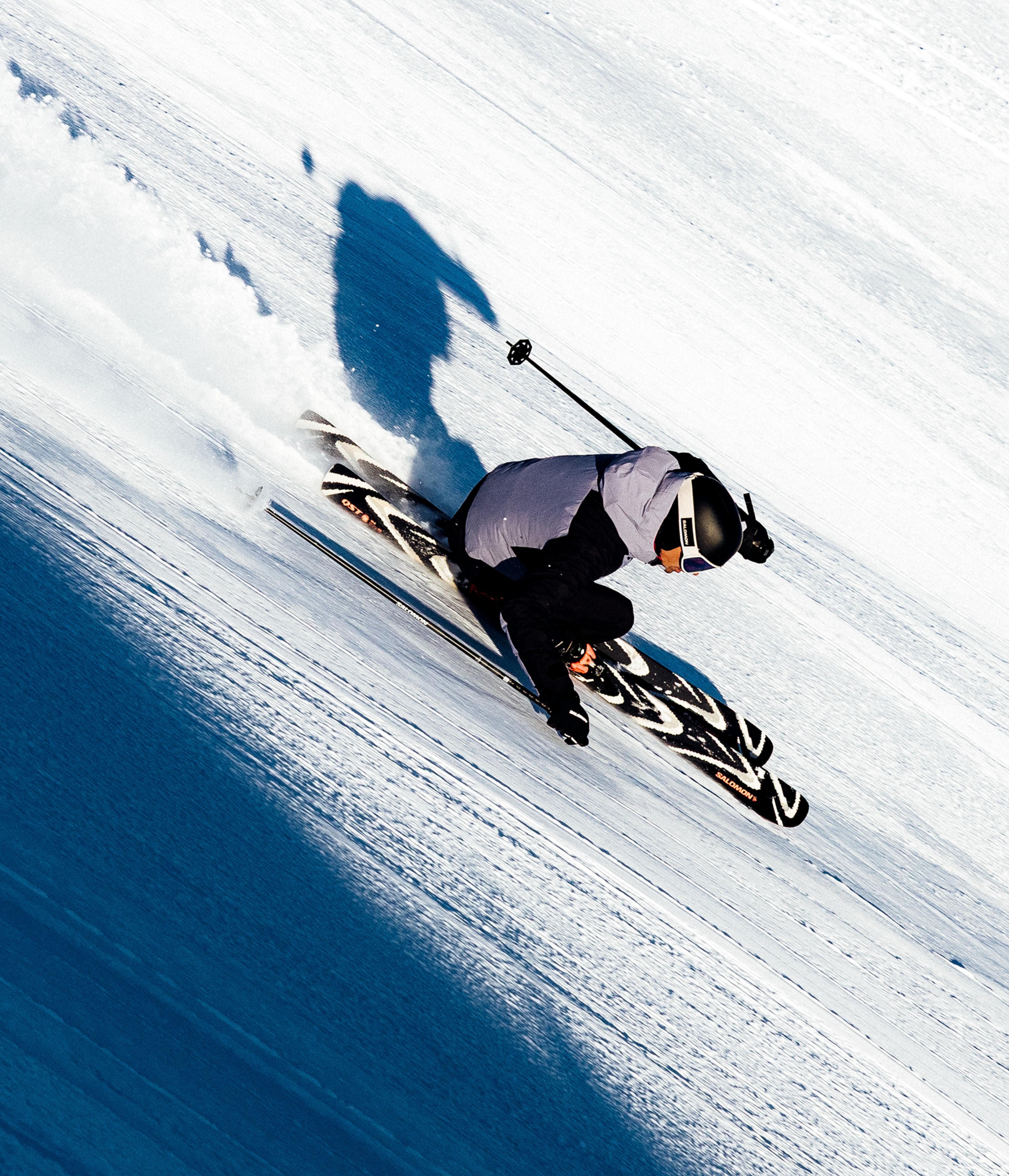 A skier turns sharply down a snowy slope, kicking up powder.