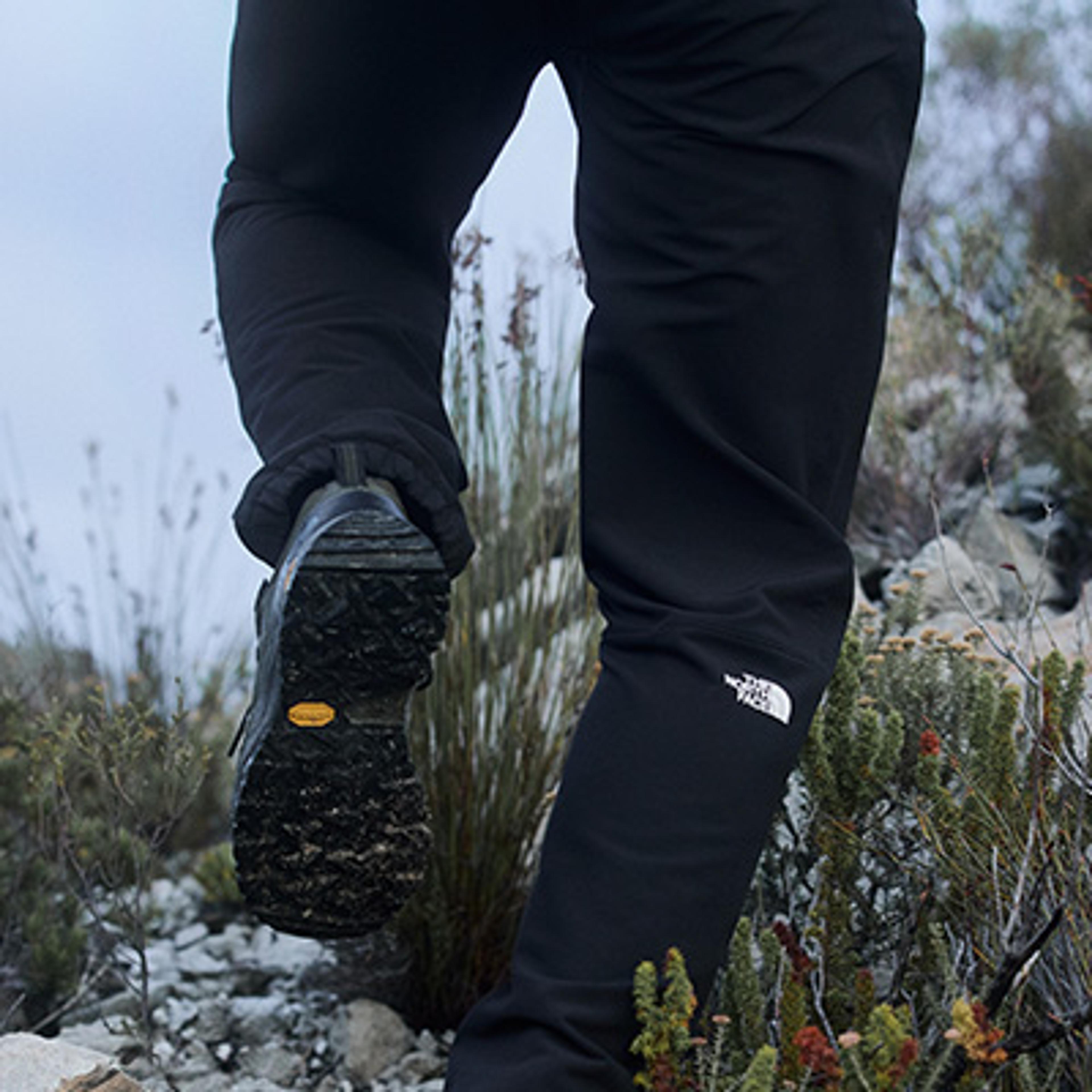 a person wearing black pants and black shoes is walking through a field .