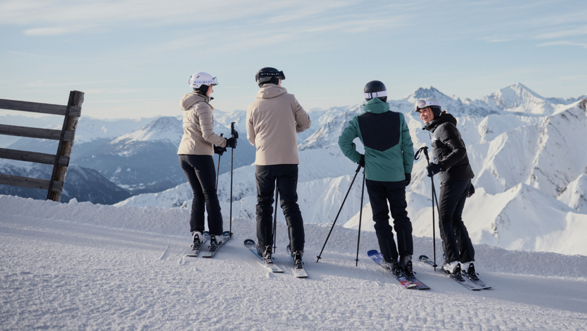 Four skiers on a snowy mountain overlooking snow-covered peaks.