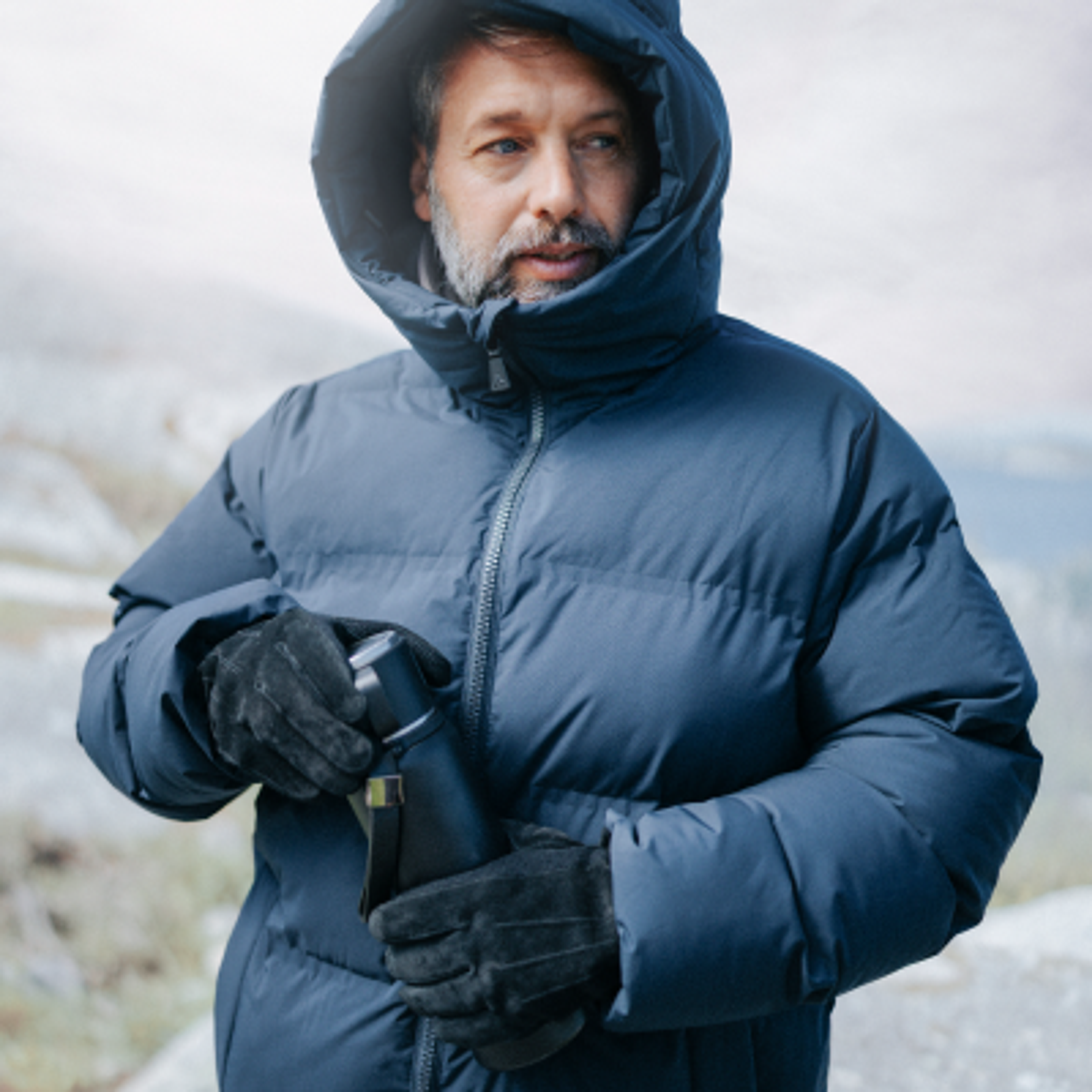 A woman in a two-tone puffer jacket and a man in a two-tone fleece jacket hiking in a blurred forest.
