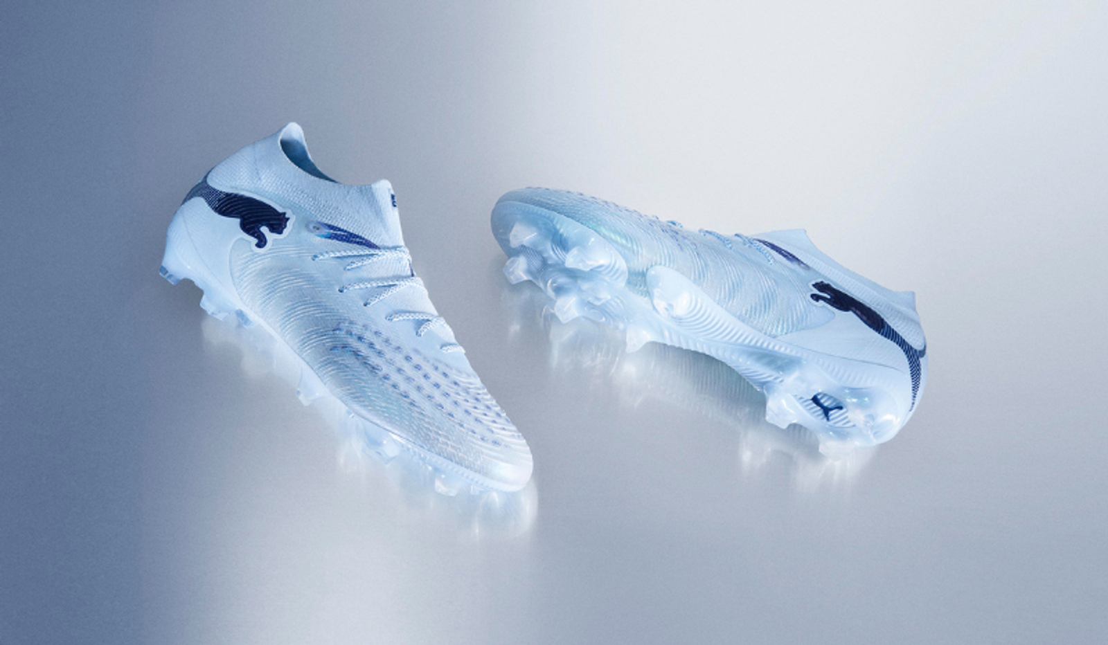 Two light blue Puma soccer cleats with black logos on a reflective surface.