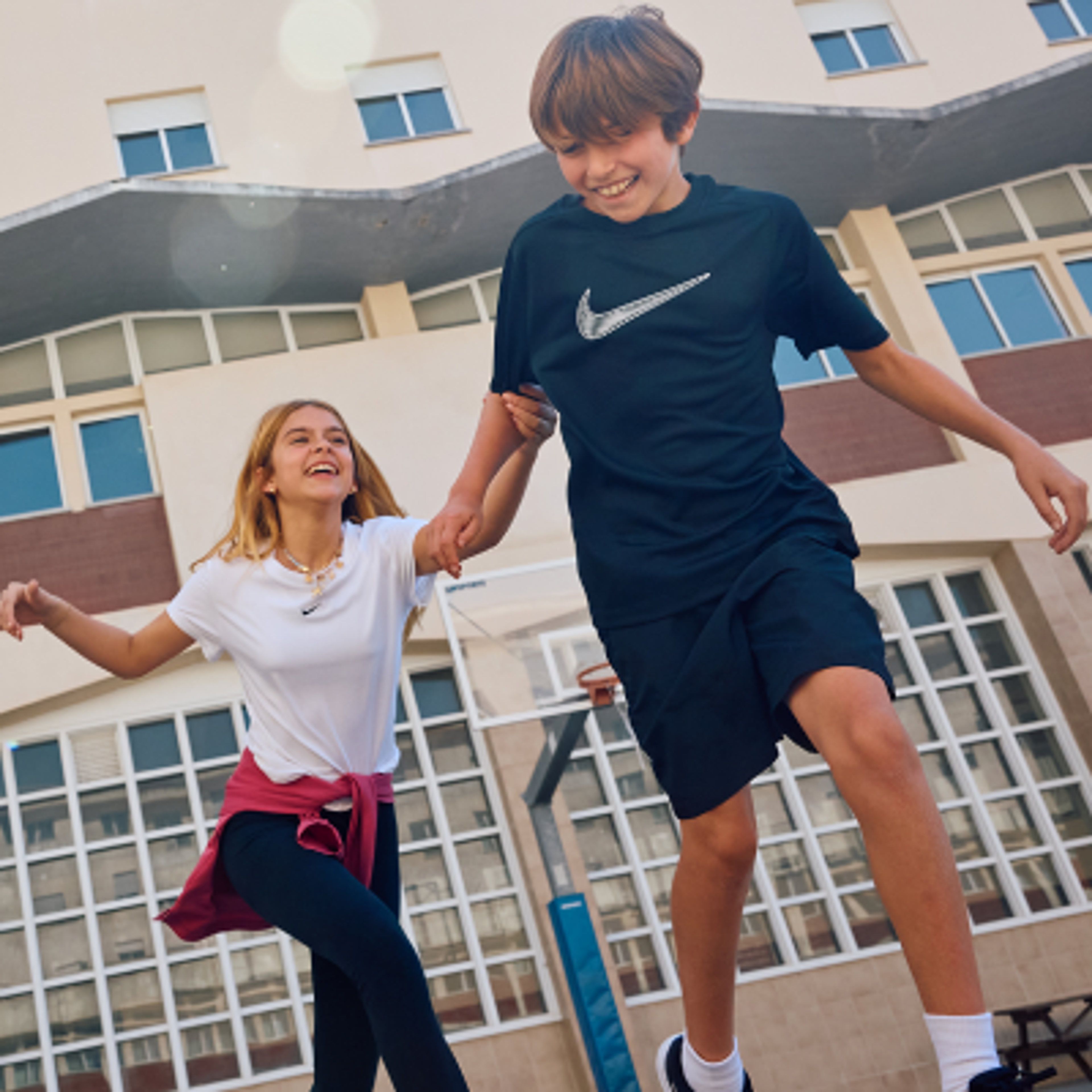Two smiling children running together, holding hands.