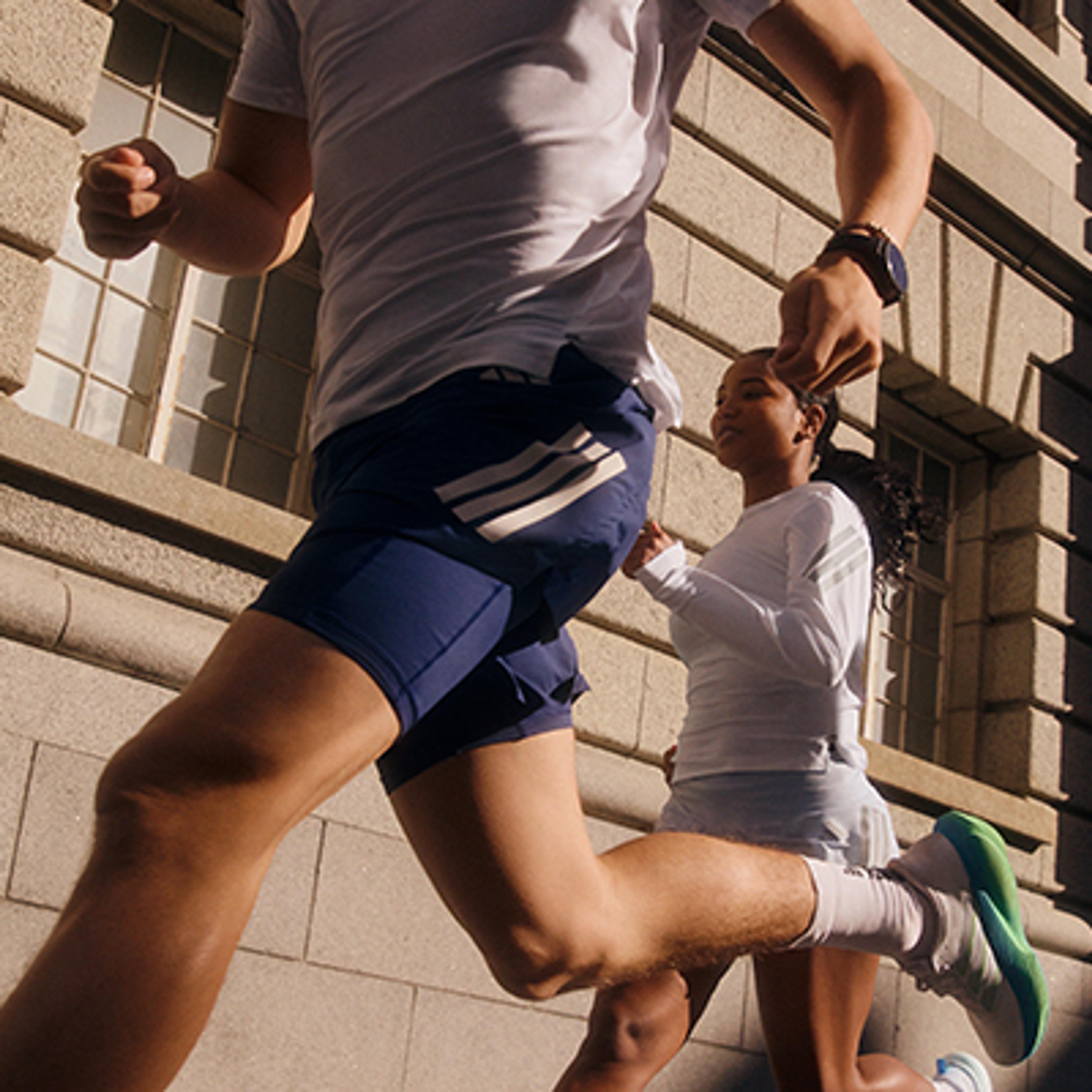 A man and woman run in athletic wear past a stone building.
