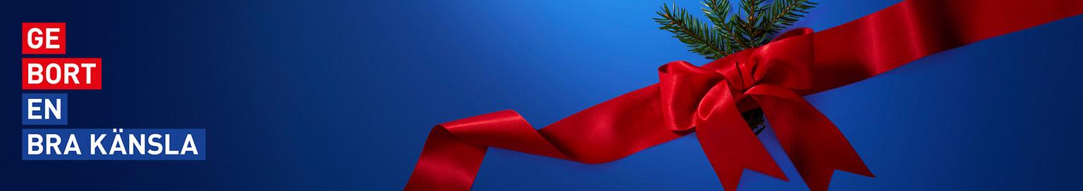 Red ribbon with a bow and evergreen sprigs on a blue background. Text: GE BORT EN BRA KÄNSLA.