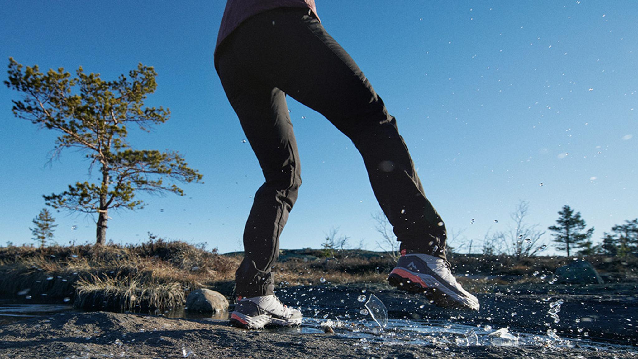 A person's hiking shoes breaking through thin ice, splashing water.