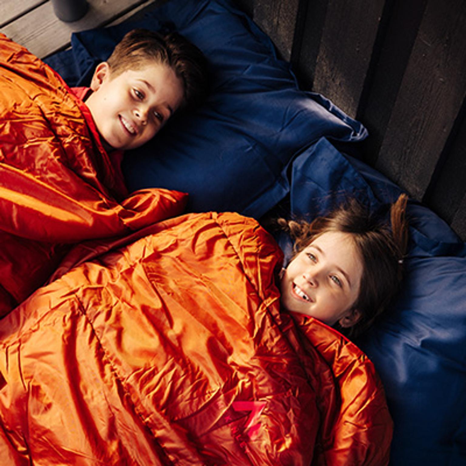 a boy and a girl are laying in sleeping bags on a bed .