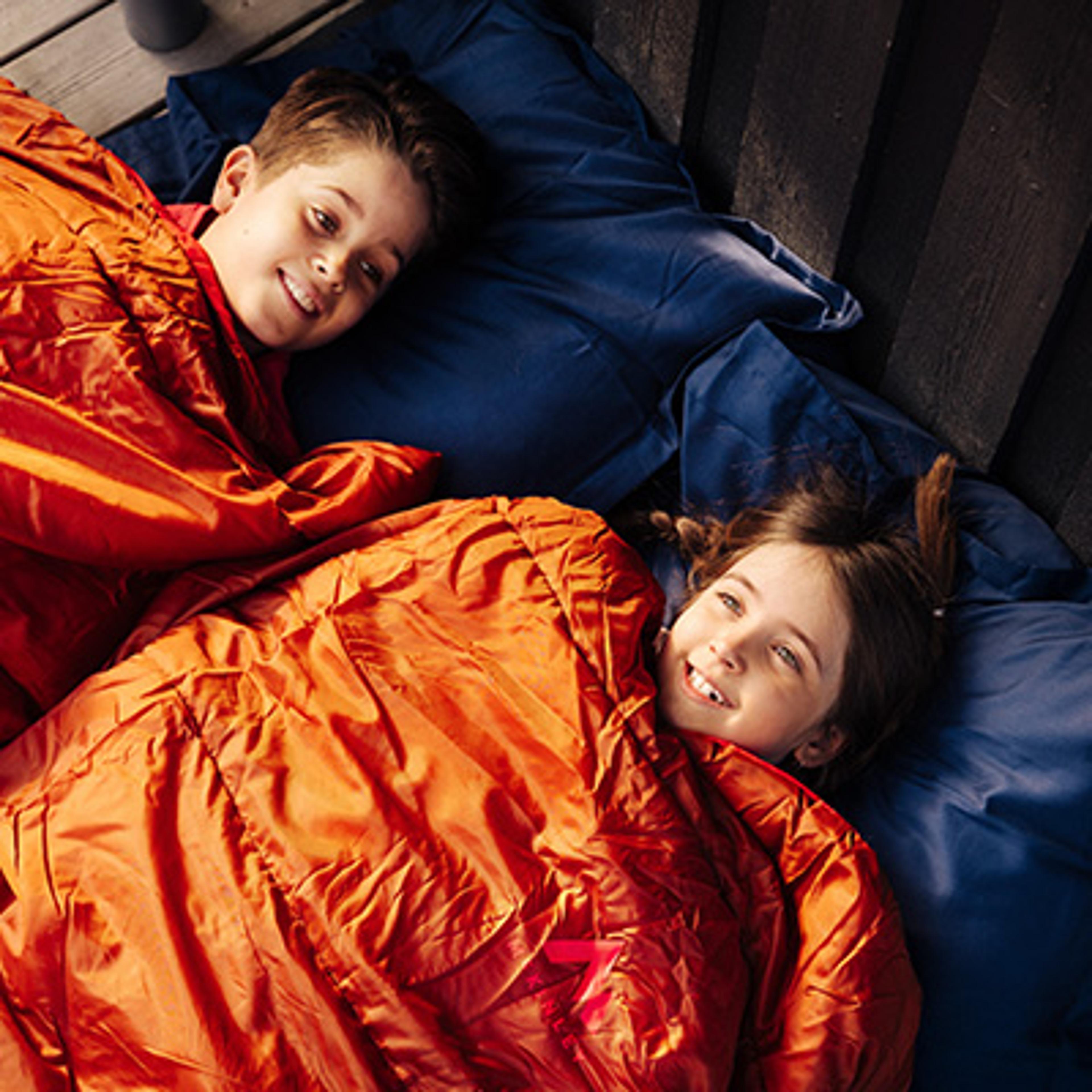 a boy and a girl are laying in sleeping bags on a bed .