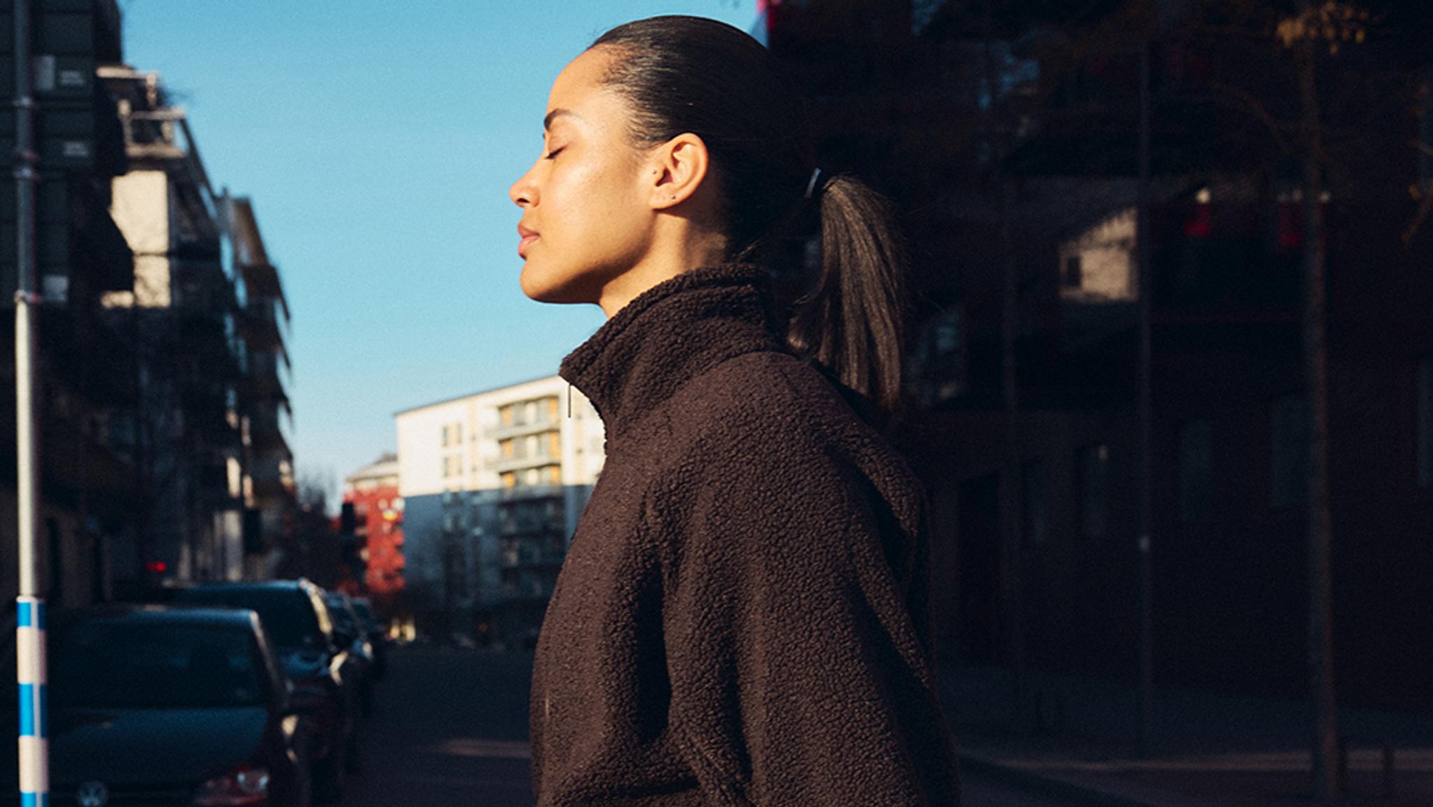 a woman is standing on a city street with her eyes closed .