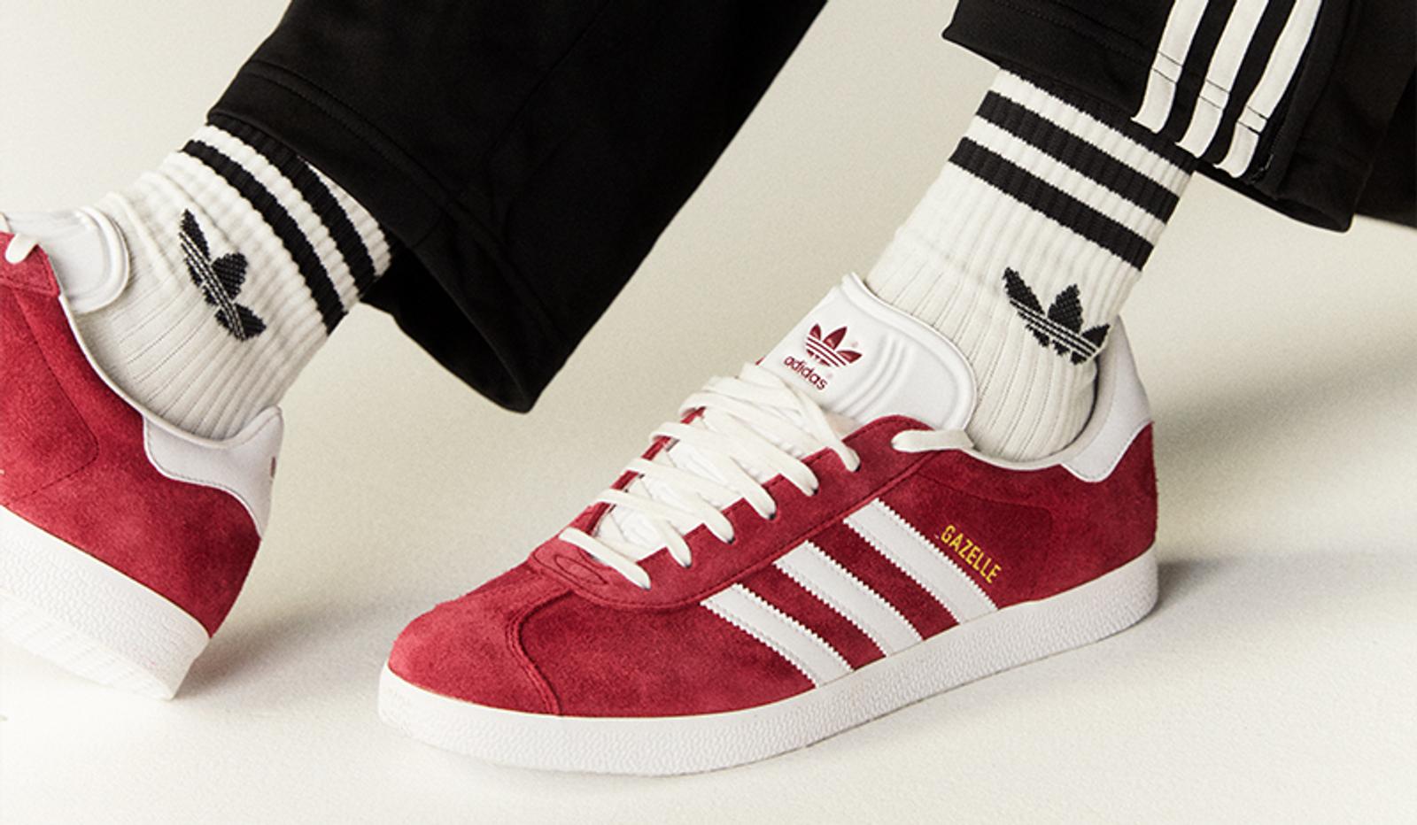 a person is wearing a pair of red and white adidas gazelle sneakers .