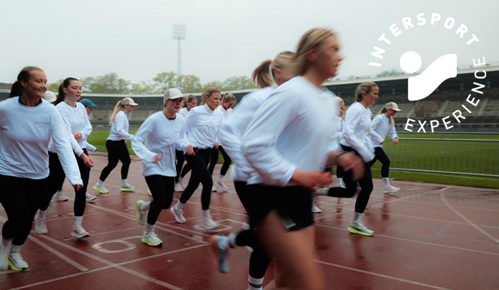 Group of women in white long-sleeved shirts running on a track, with an Intersport Experience logo.