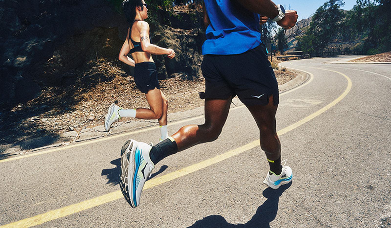 Two runners on a sunny winding road, their running shoes prominent.