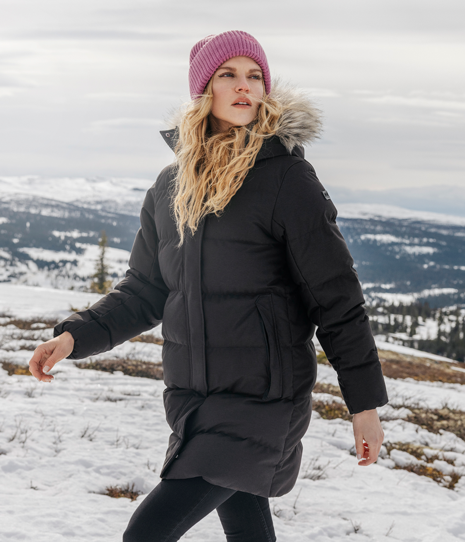 a woman wearing a black coat and a pink hat is standing in the snow