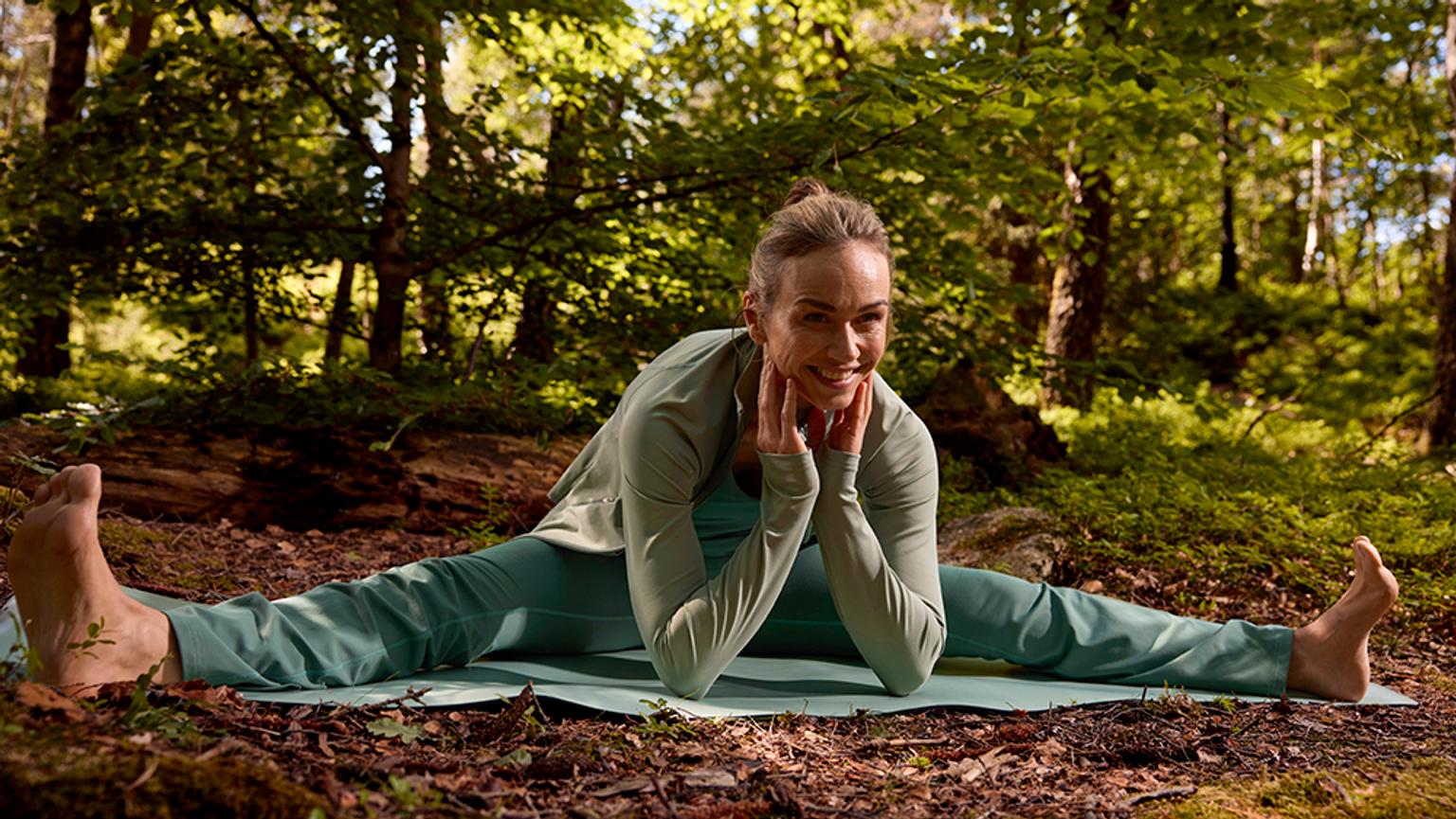 a woman is doing a split on a yoga mat in the woods .