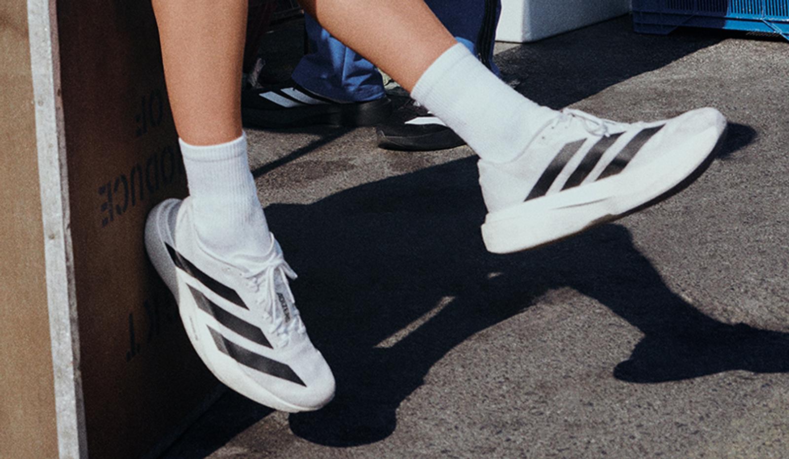 a person wearing a pair of white and black adidas shoes .