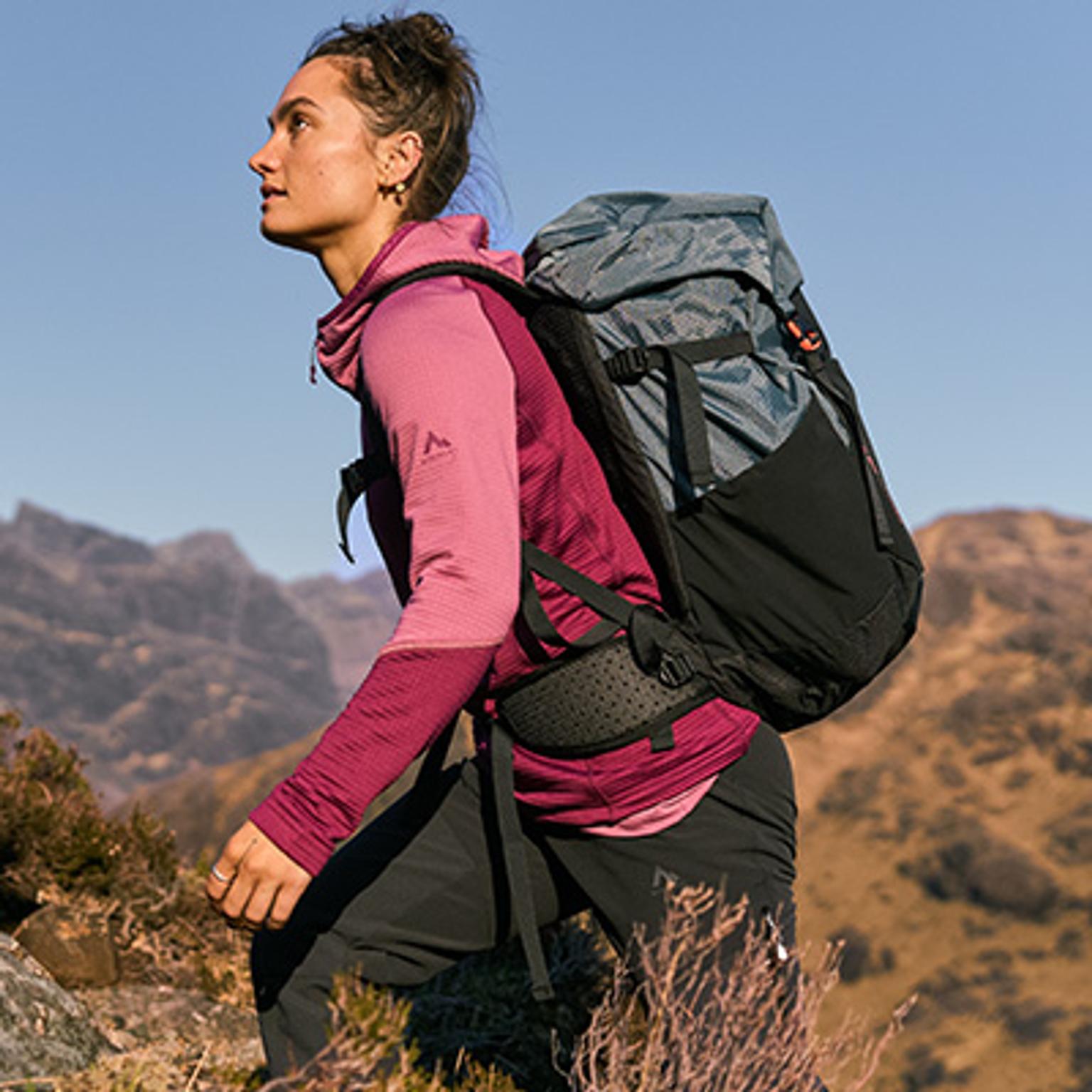 a woman is hiking in the mountains with a backpack .