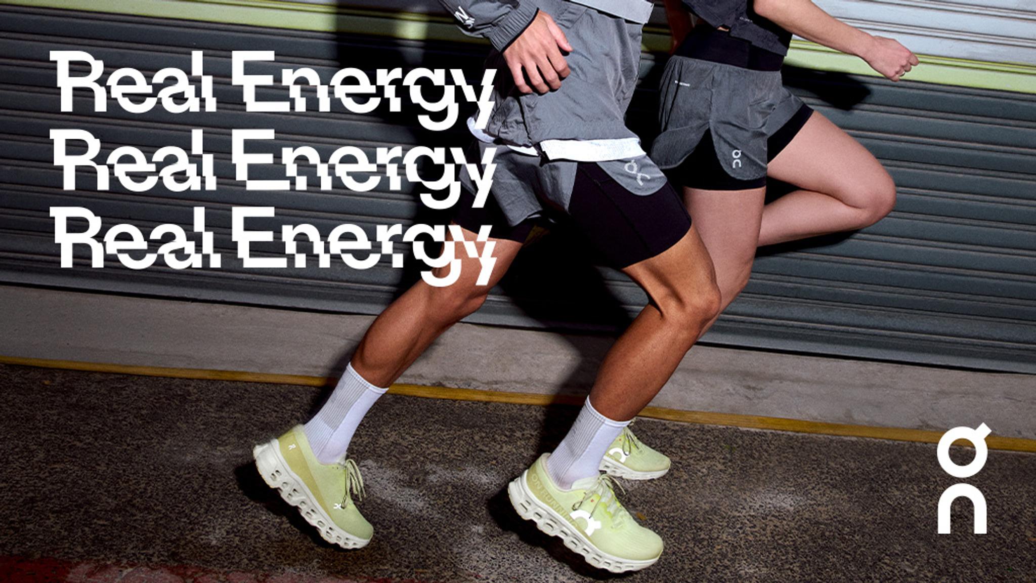 Two runners in light green shoes and athletic shorts in motion on an urban street. "Real Energy" text is repeated three times on the left, with an "on" logo on the right.