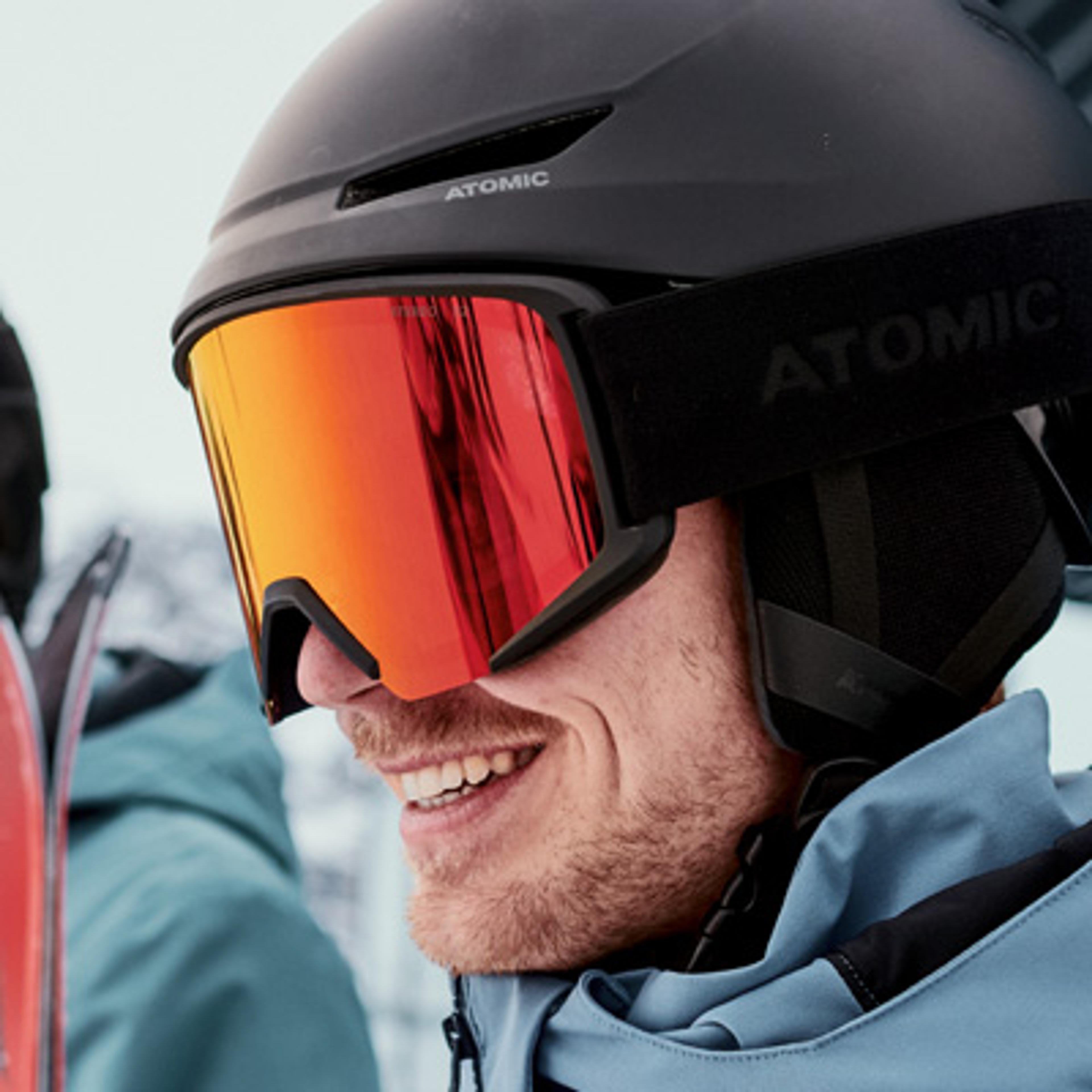 Smiling man wearing a black Atomic ski helmet and red mirrored goggles.