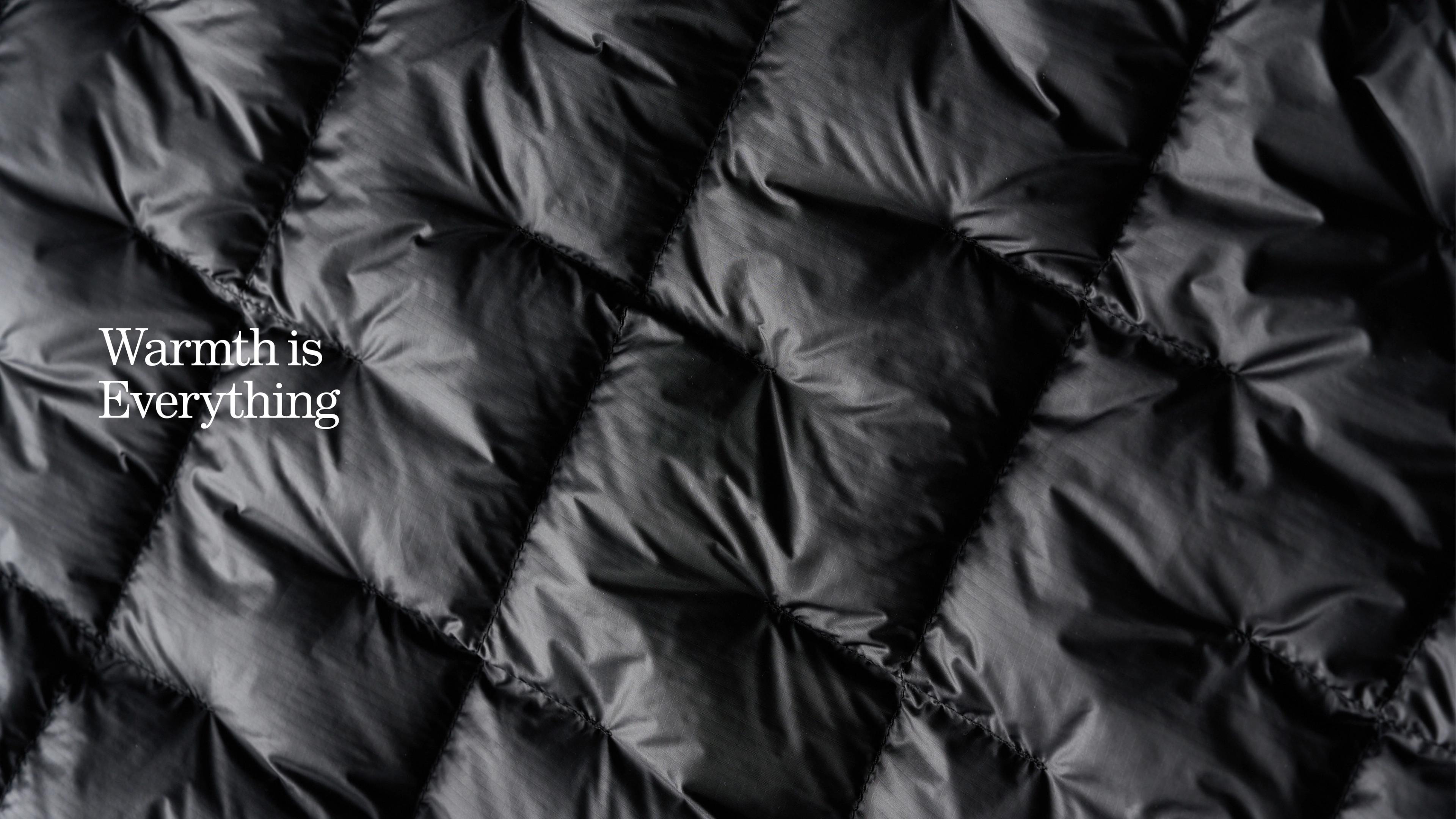 a close up of a black padded jacket with the words `` warmth is everything '' written on it .