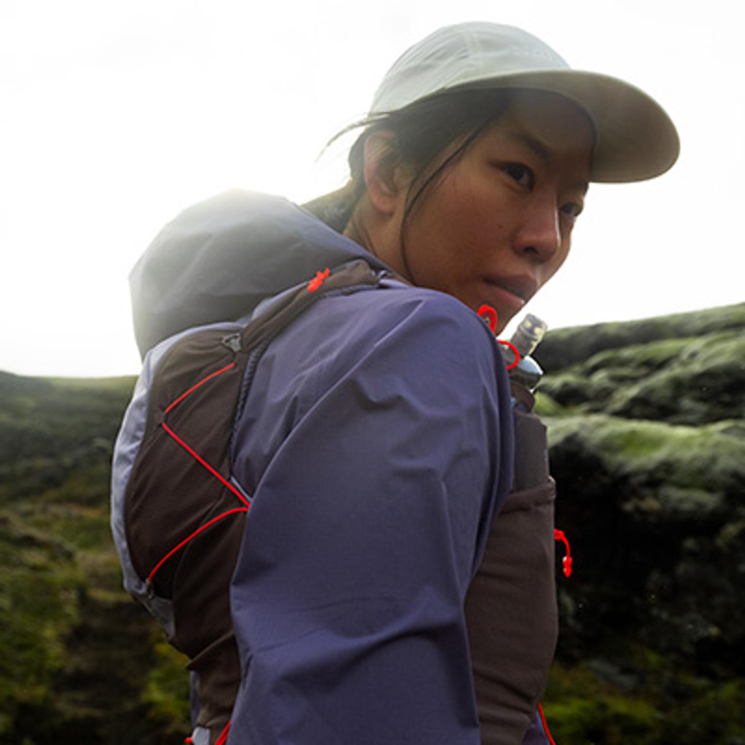 Person wearing cap, jacket, and running vest looks back.
