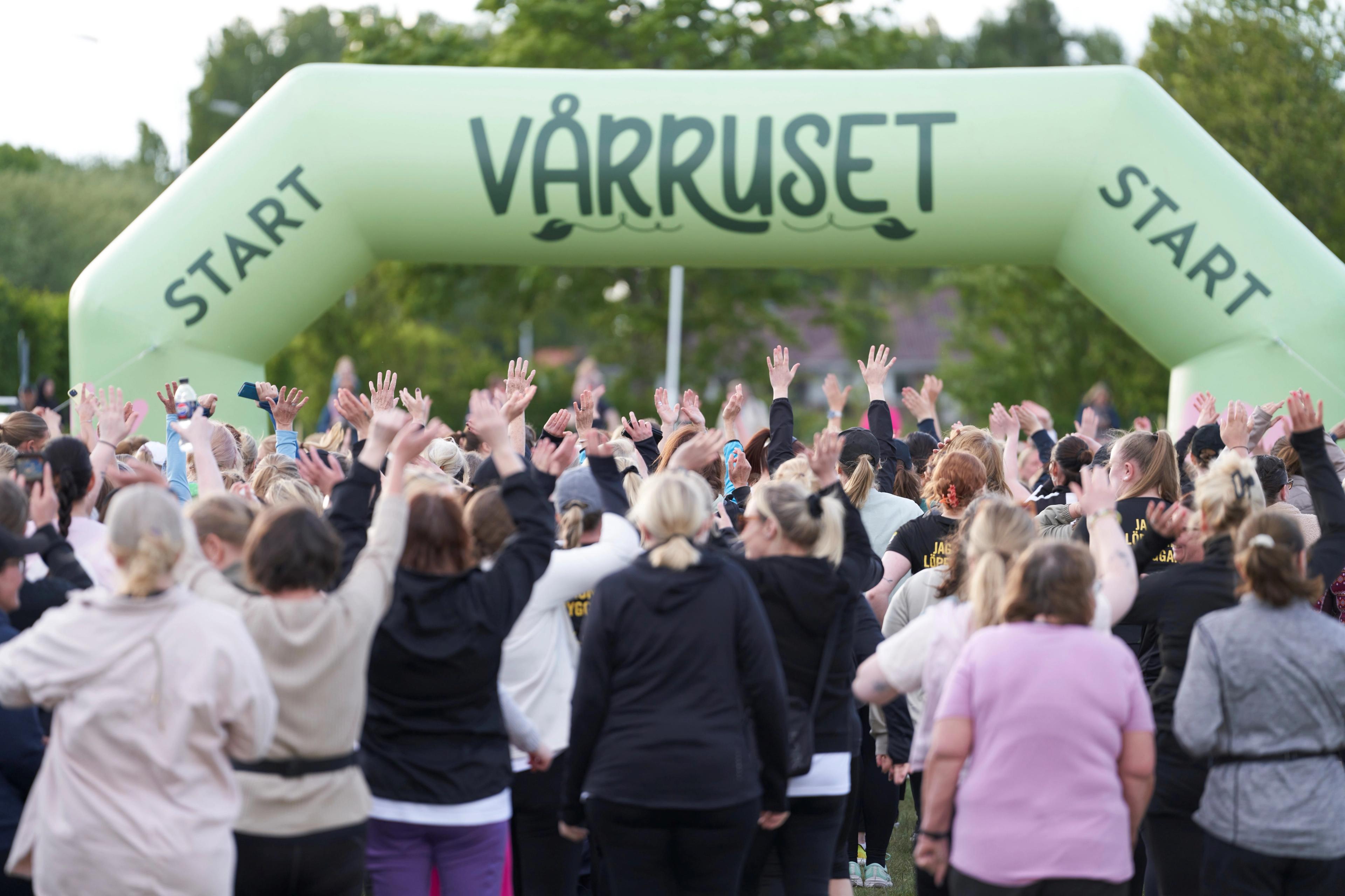 A large group of people with raised arms under a green "VÅRRUSET START" arch.