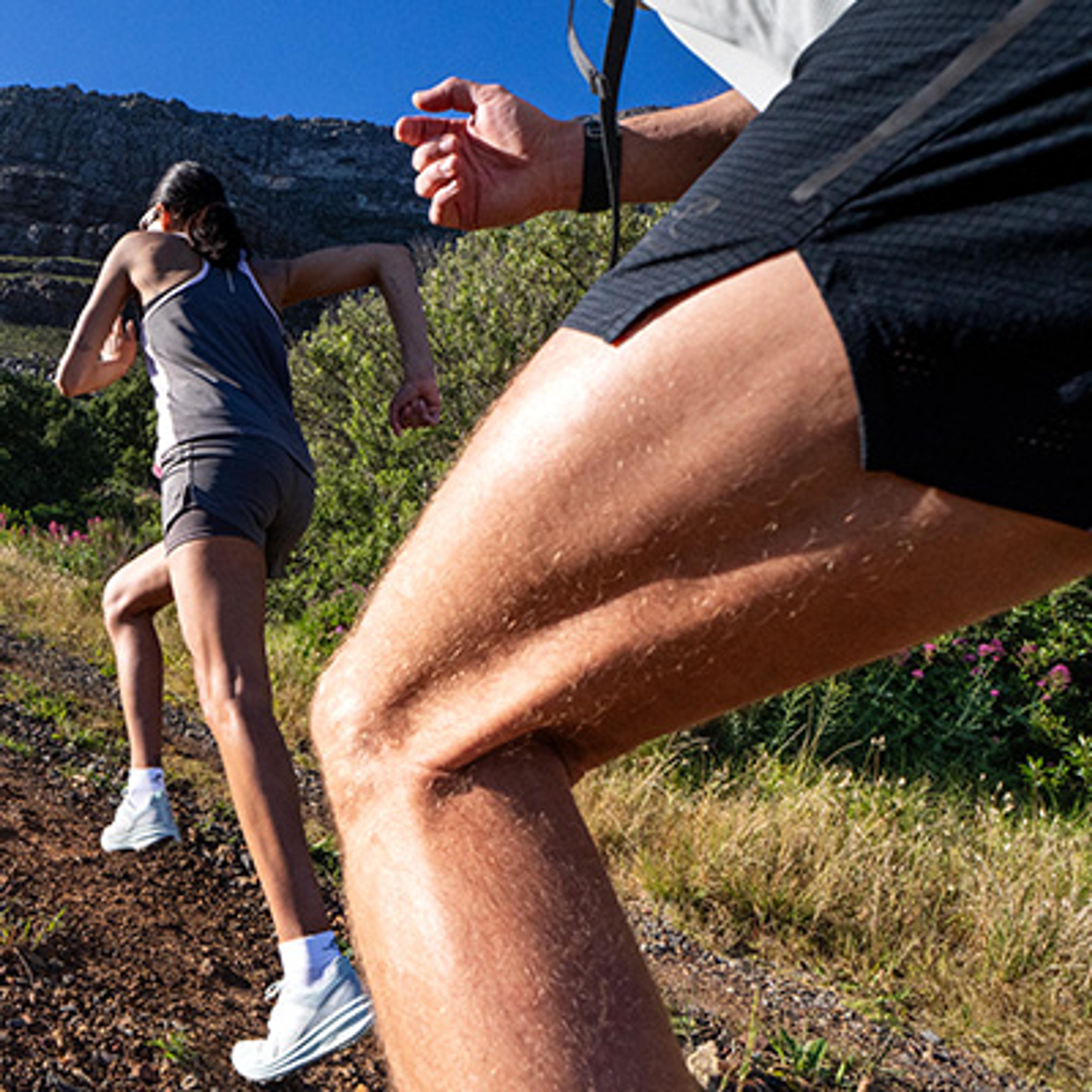 Two runners ascend a sunny mountain trail.