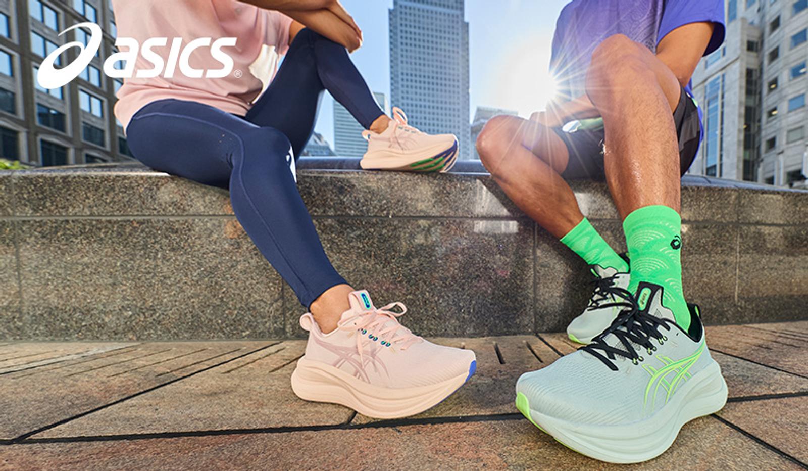Two individuals sitting, showcasing pink and light blue Asics running shoes in an urban setting.