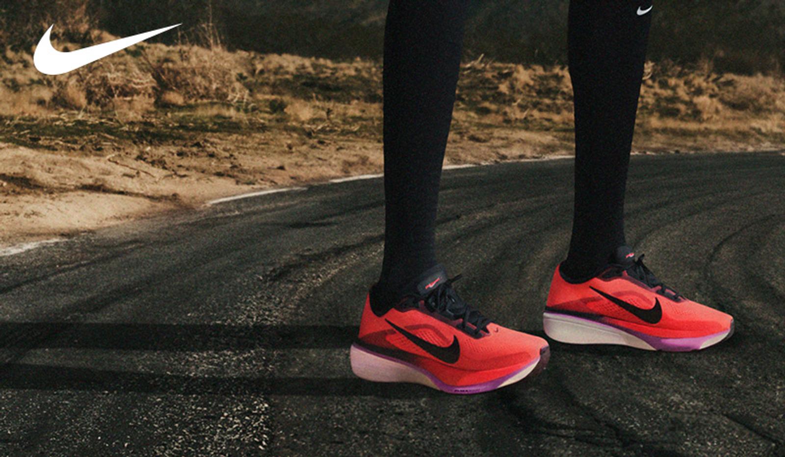 A person wears red Nike running shoes and black socks on an asphalt road. A Nike logo is in the top left.