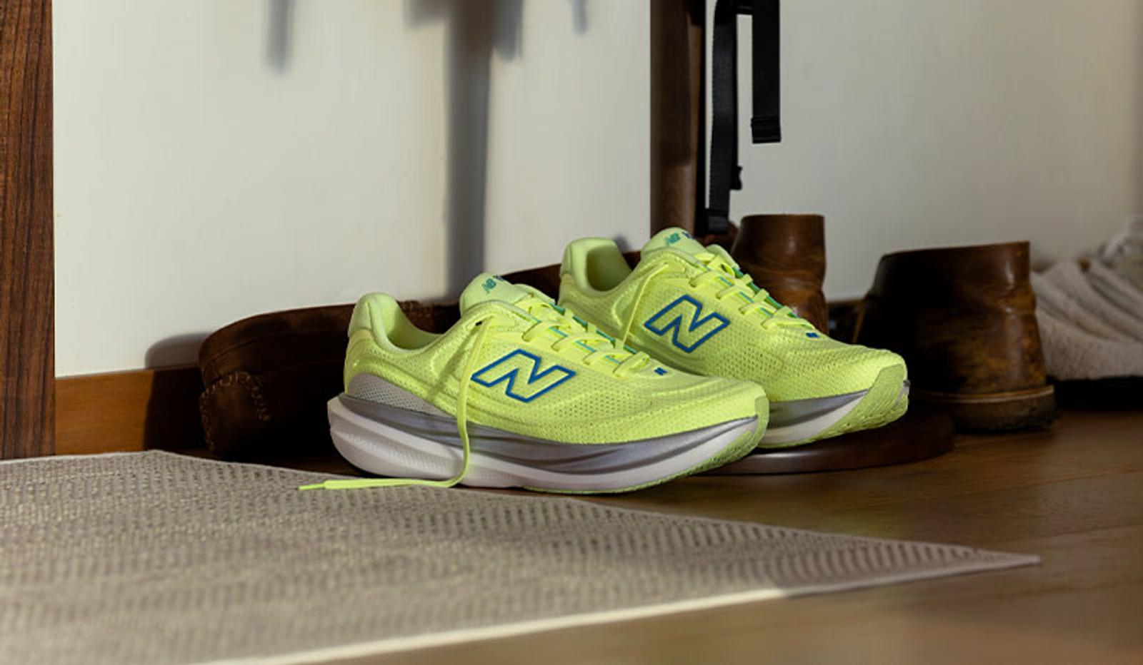 A pair of lime green New Balance sneakers with blue logos and thick grey and white soles, on a wooden floor next to a rug.