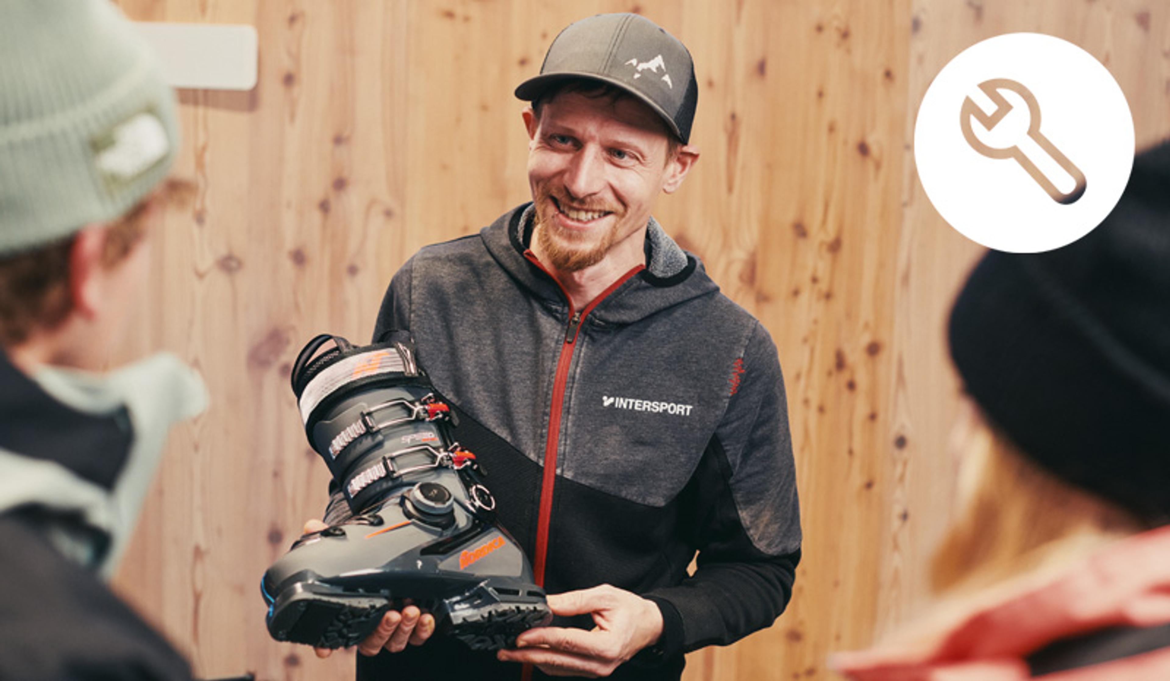 A smiling man in an Intersport hoodie holds a ski boot, presenting it to two people, with a wrench icon in the top right.