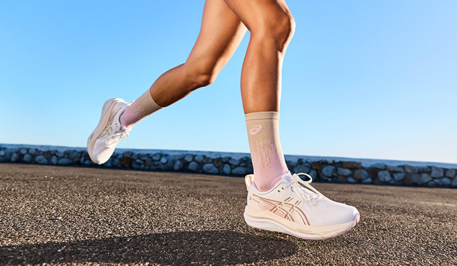 A person's legs in white running shoes and beige-pink gradient socks striding on pavement.