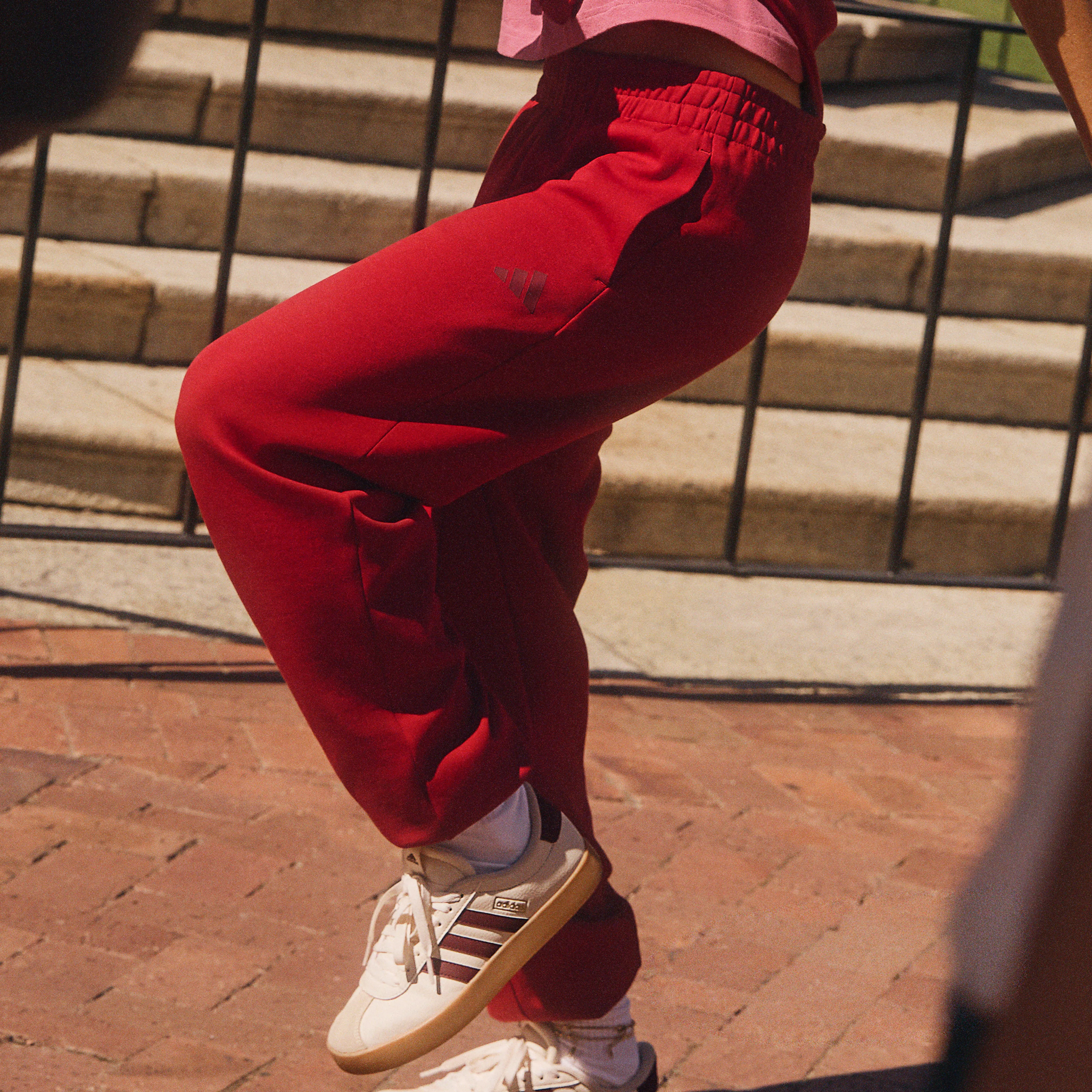 A young woman in a pink top and red pants juggles a colorful soccer ball outdoors, flanked by two other partially visible people.