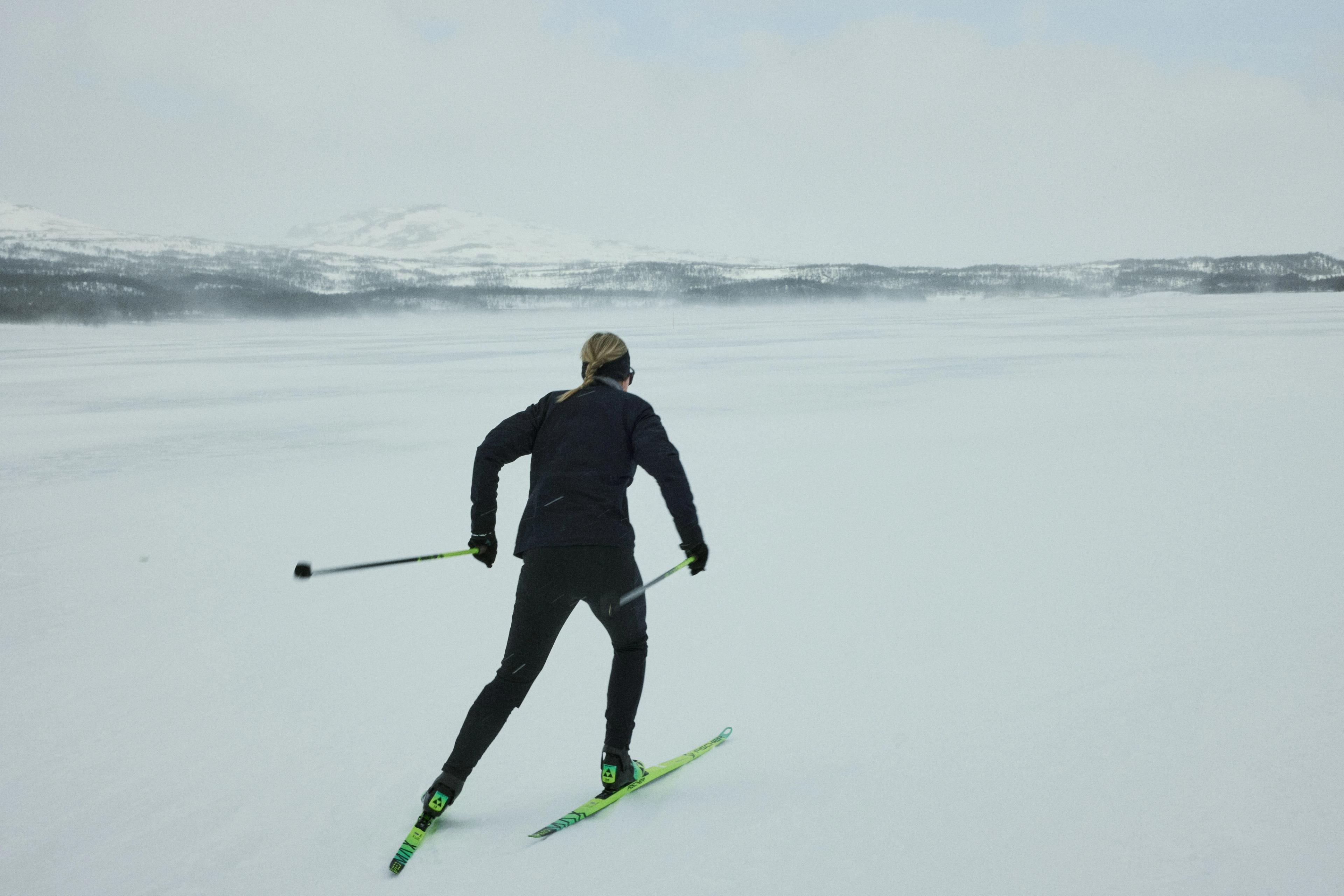 A person cross-country skiing on a wide, snowy plain with distant mountains.