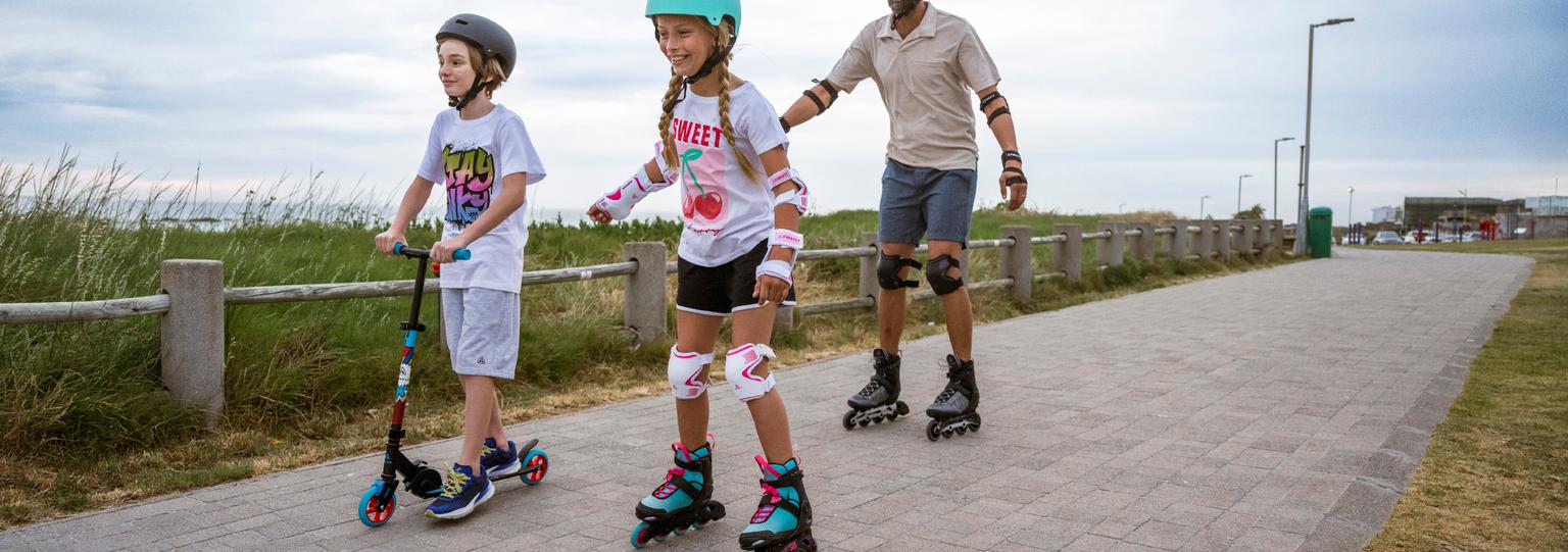 En vuxen och två barn åker inlines och sparkcykel