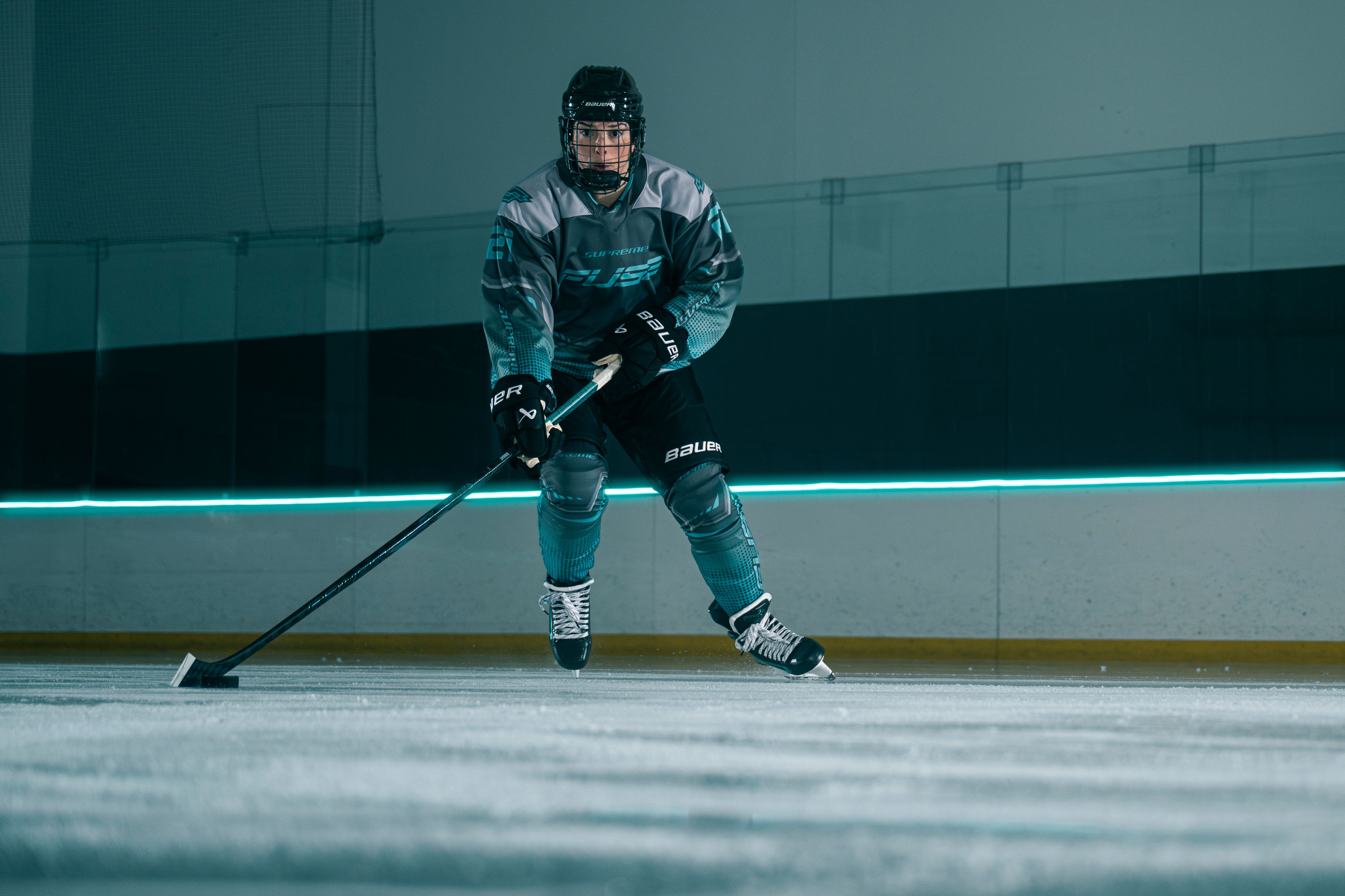 A hockey player in a teal and grey uniform skates on an ice rink, holding a stick.