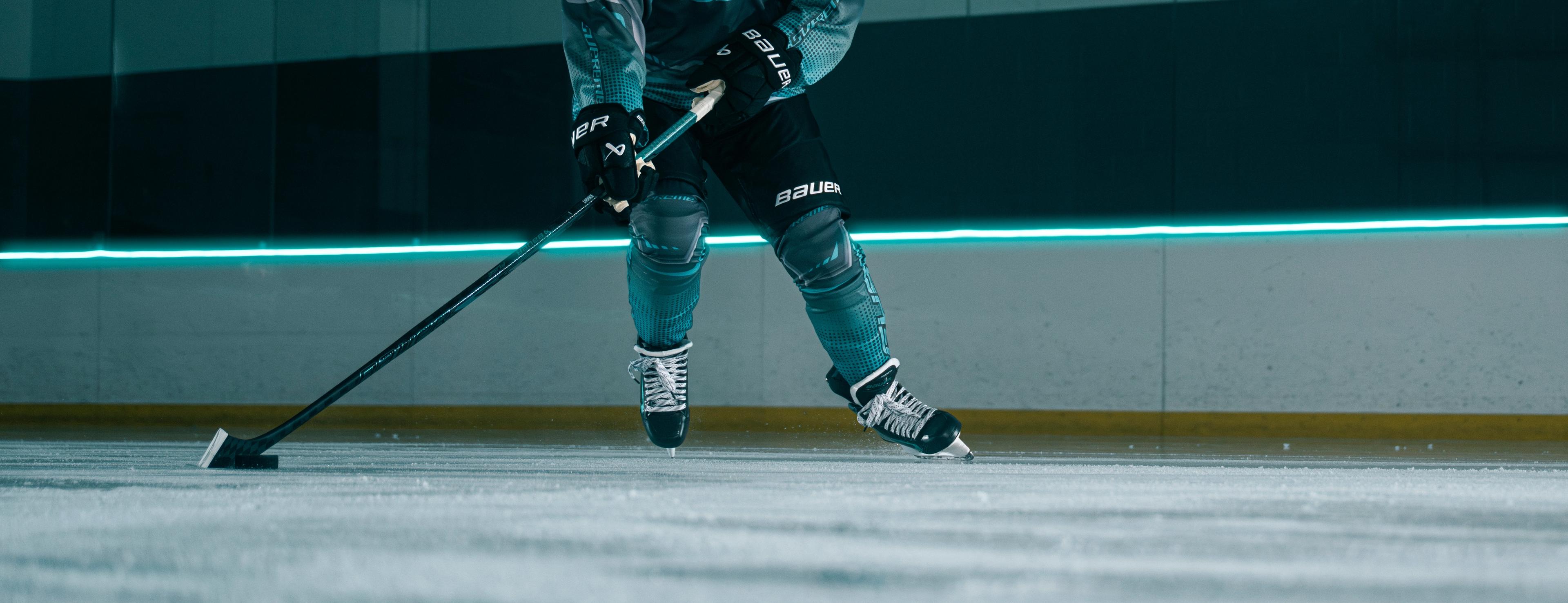A hockey player in a teal and grey uniform skates on an ice rink, holding a stick.