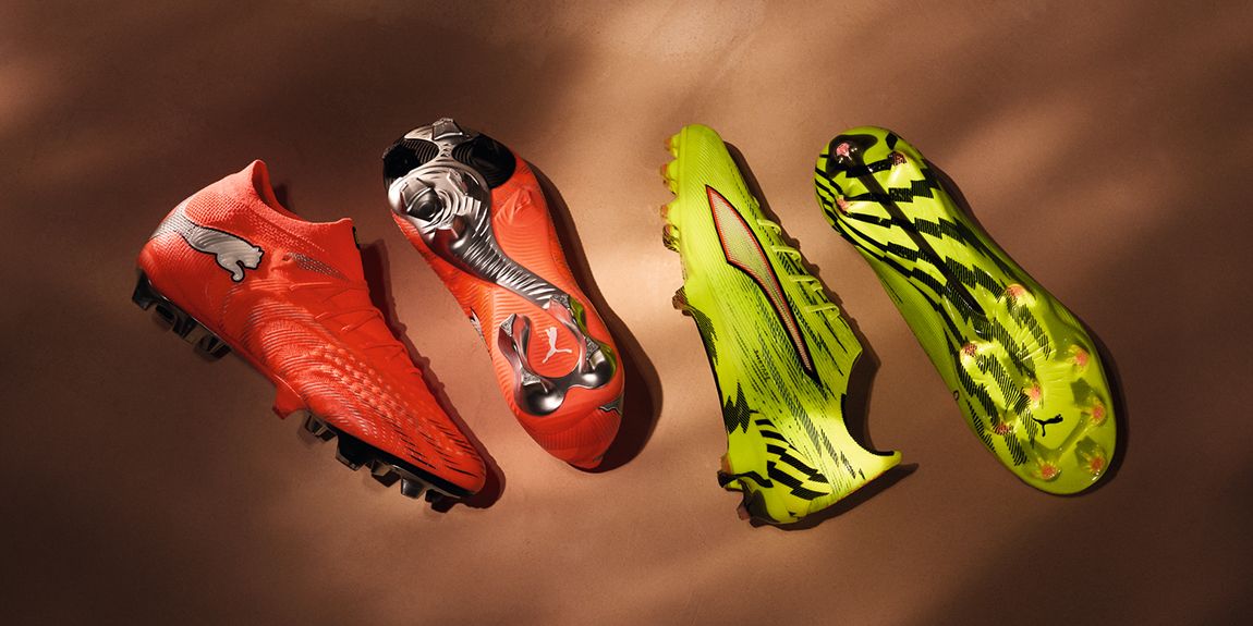 Four Puma soccer cleats, two orange and two neon green, on a brown surface.