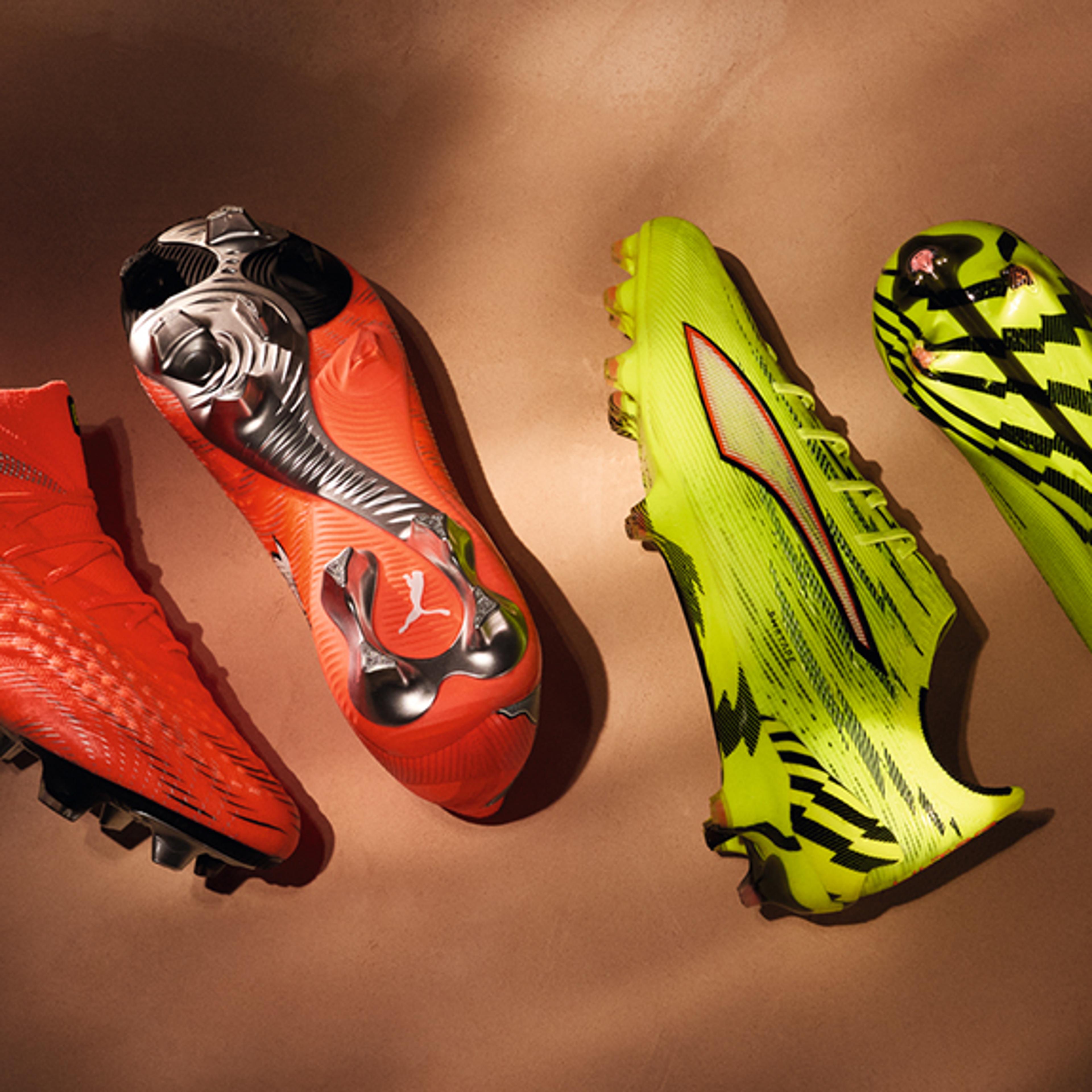 Two pairs of Puma soccer cleats, one orange and one neon green, on a brown background.