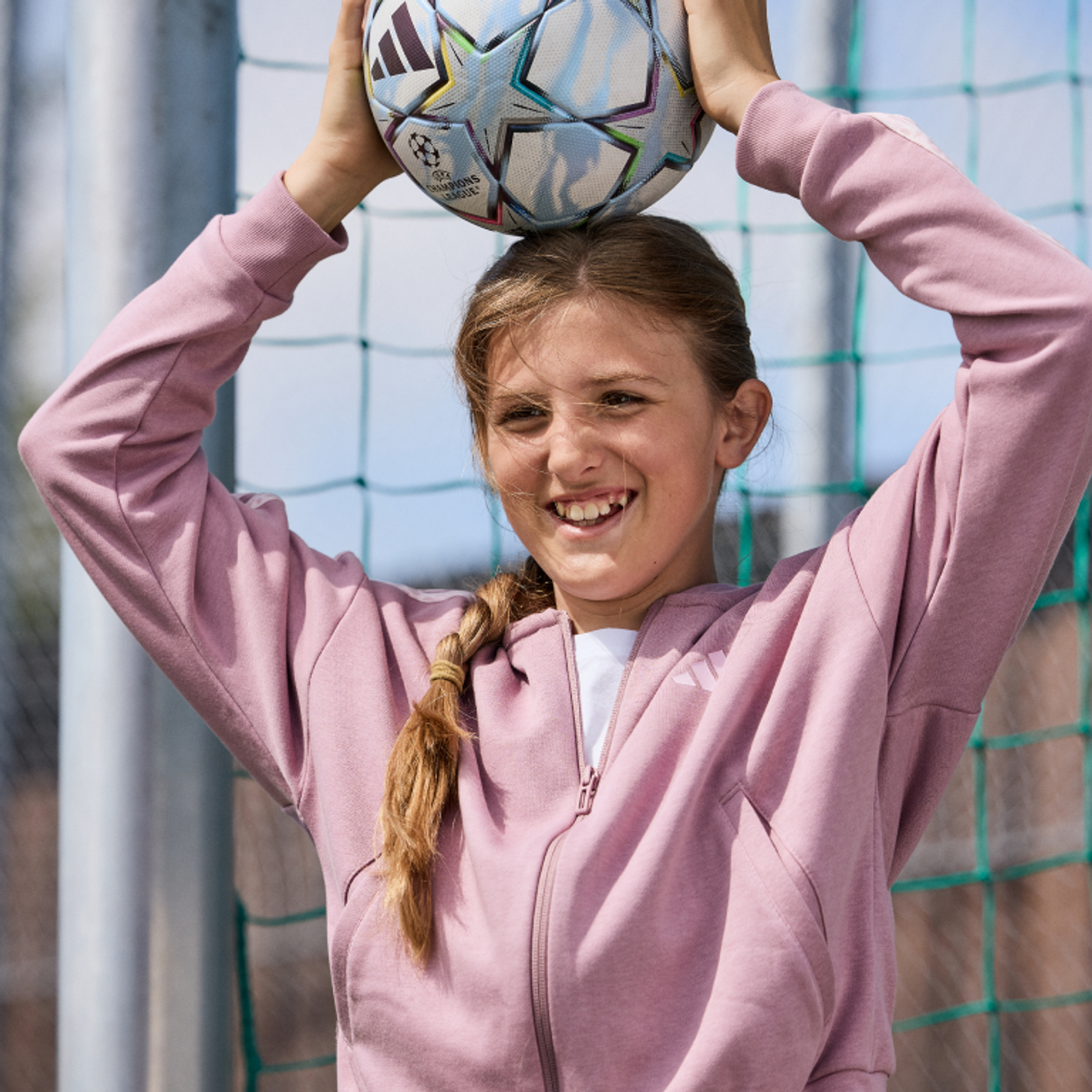 Smiling girl holding a soccer ball on her head in front of a goal net.
