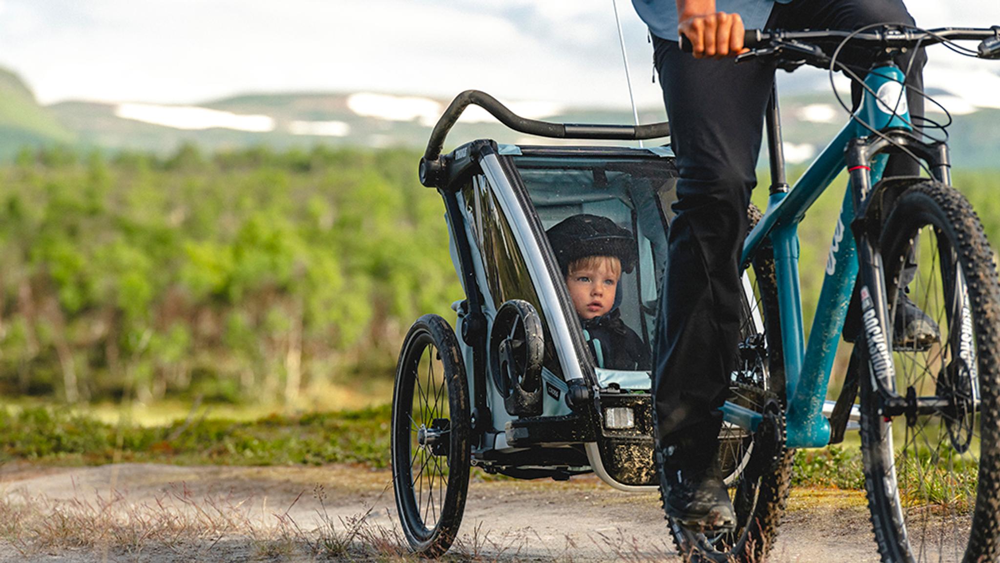 a man is riding a bike with a child in a trailer .