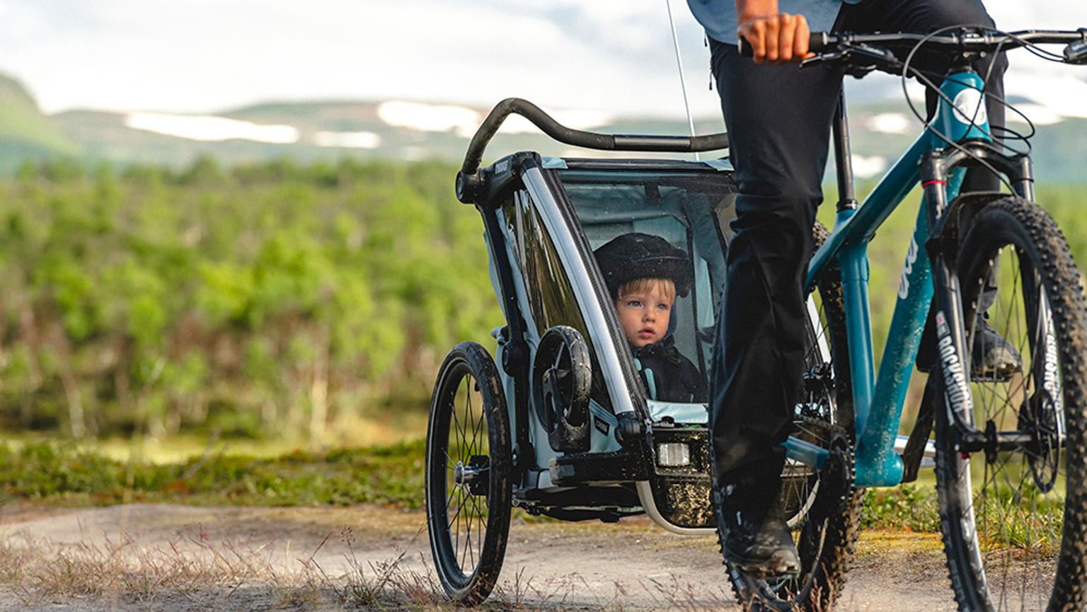 a man is riding a bike with a child in a trailer .