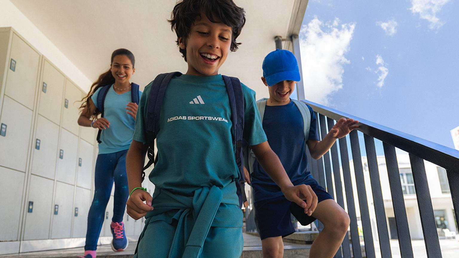 three children in sportswear are running down stairs .