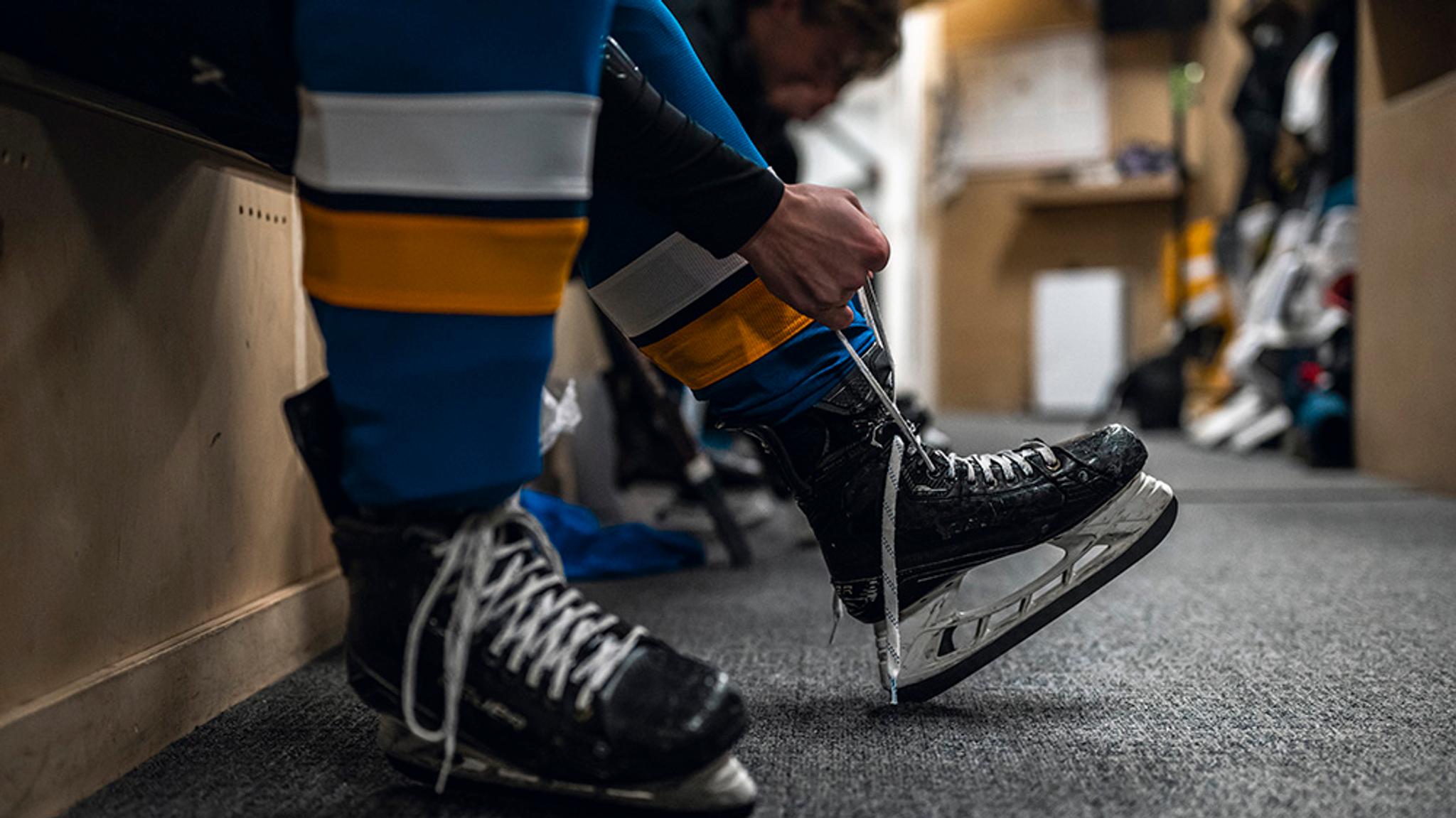 A person lacing up a hockey skate in a locker room.
