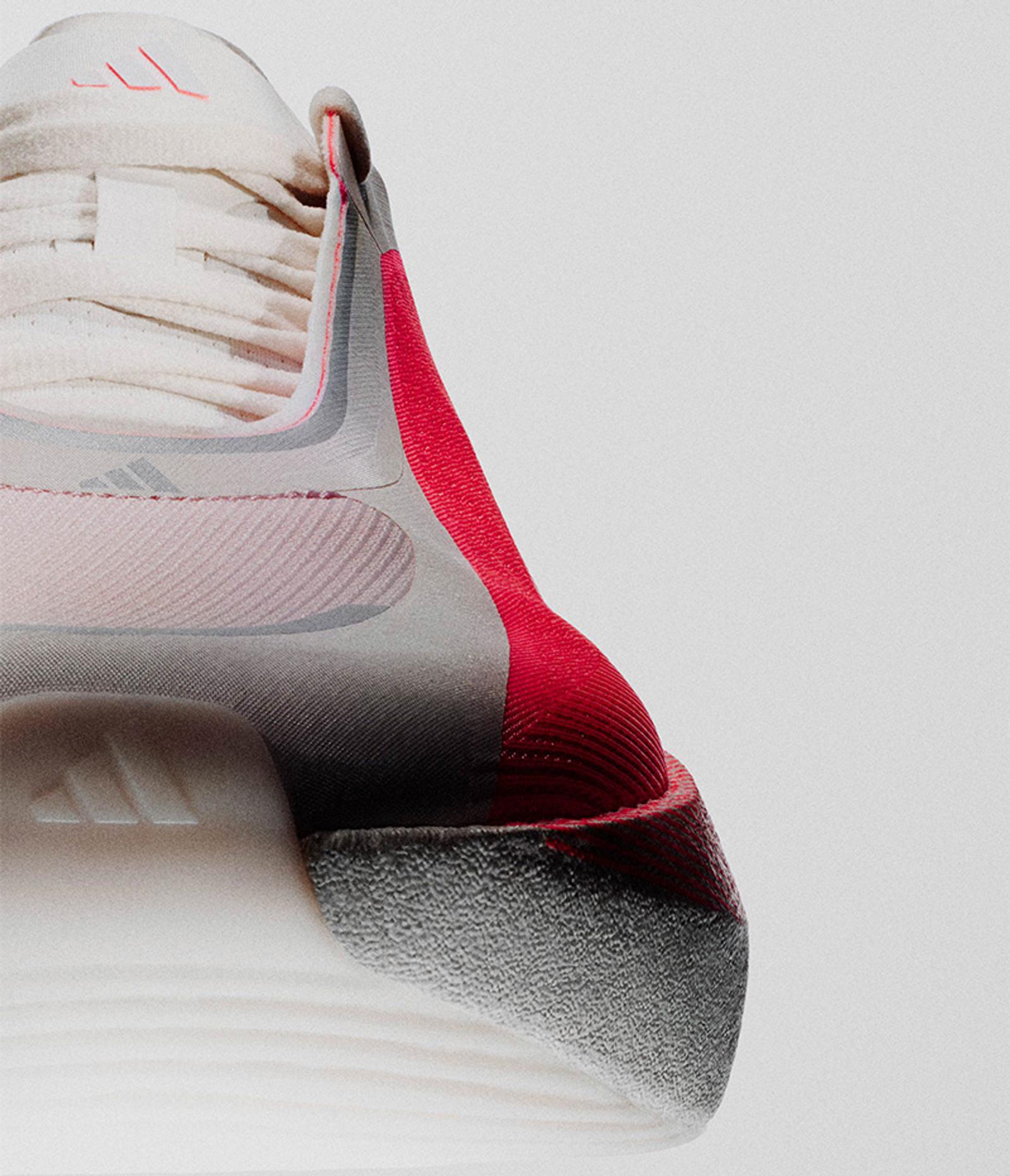 A close-up of a cream and pink Adidas athletic shoe with bright red accents and a textured grey sole.