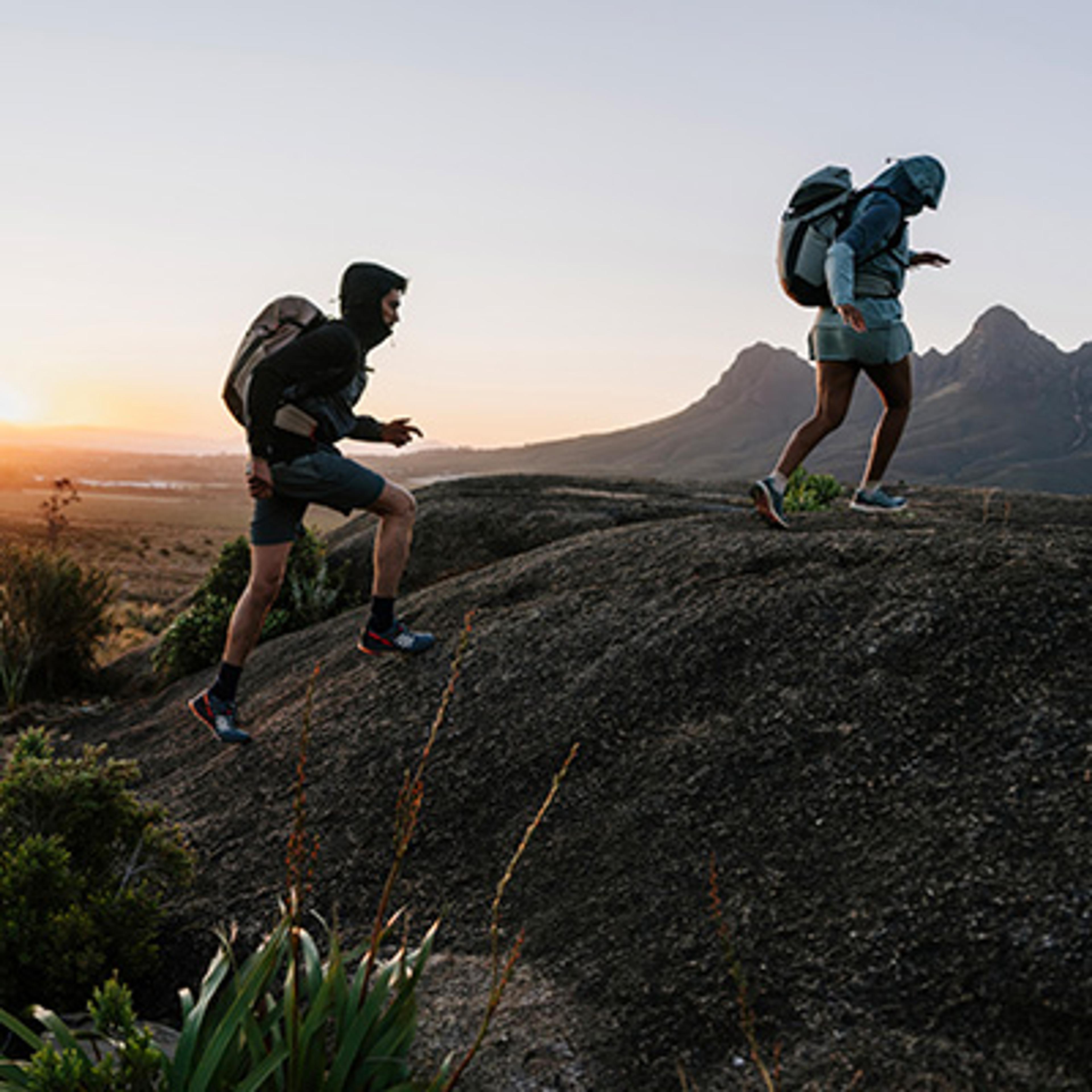 a man and a woman are hiking up a hill .