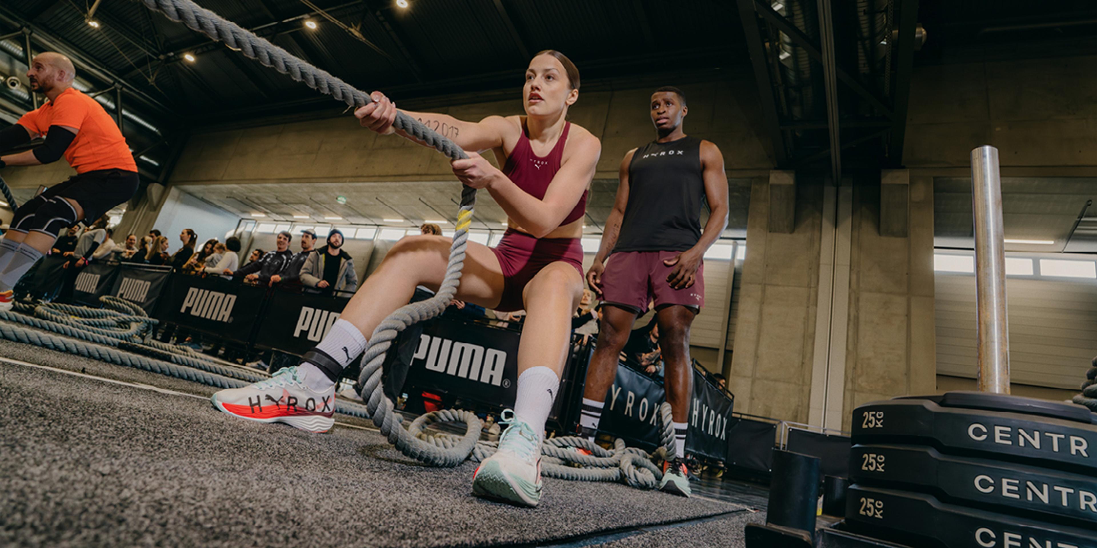 a woman is pulling a rope in a gym while a man watches .