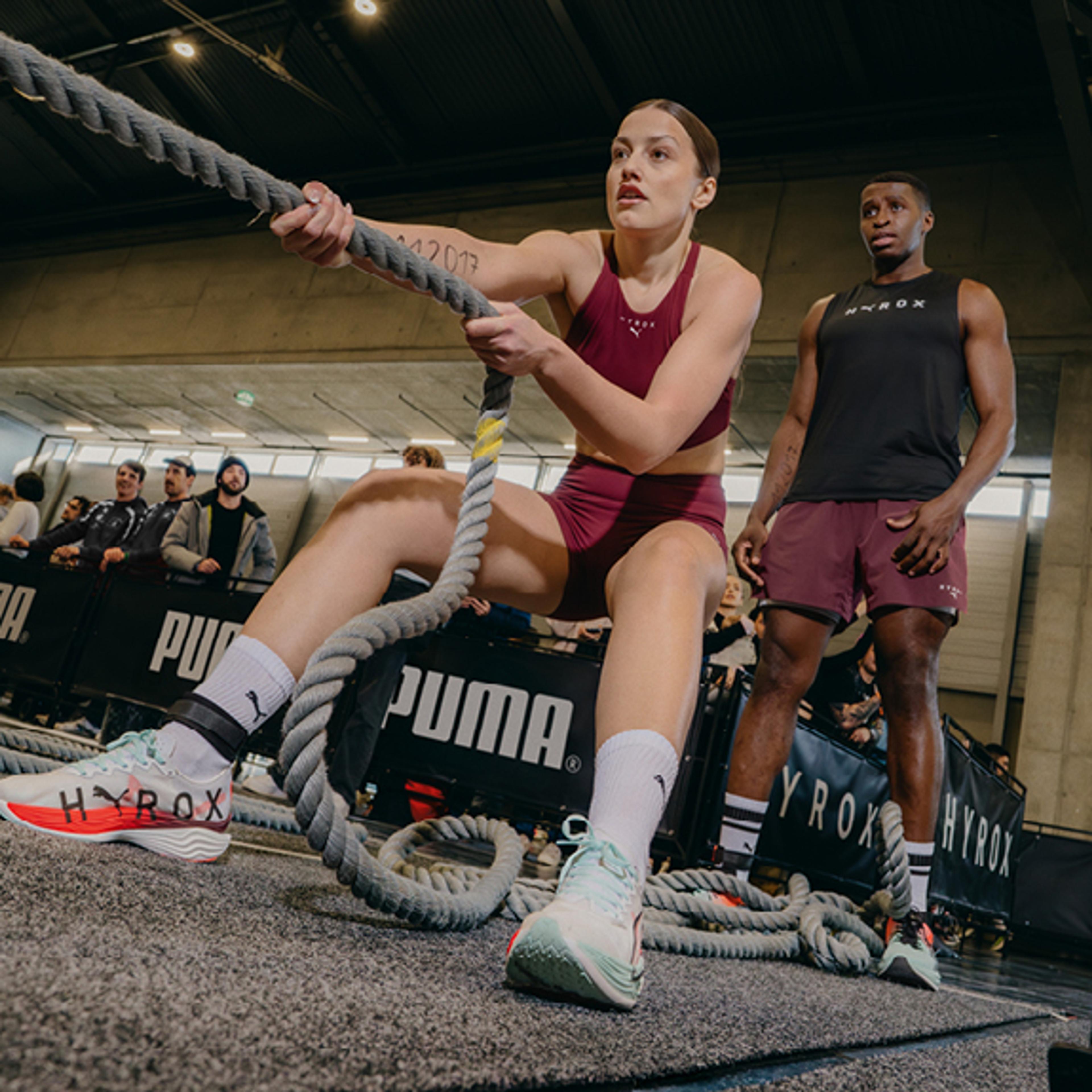a woman is pulling a rope in a gym while a man watches .