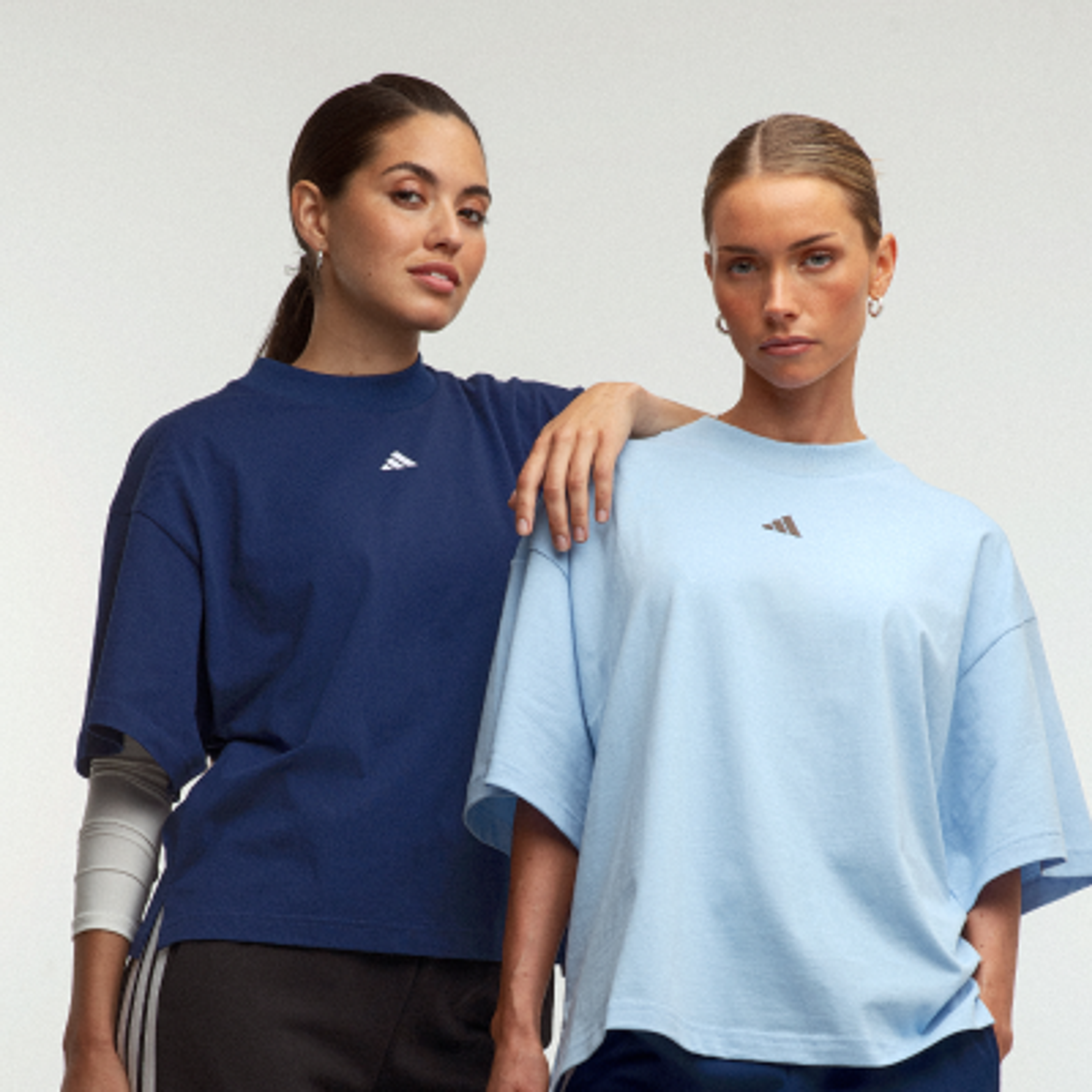 Two women wearing oversized Adidas t-shirts, one navy blue and one light blue.